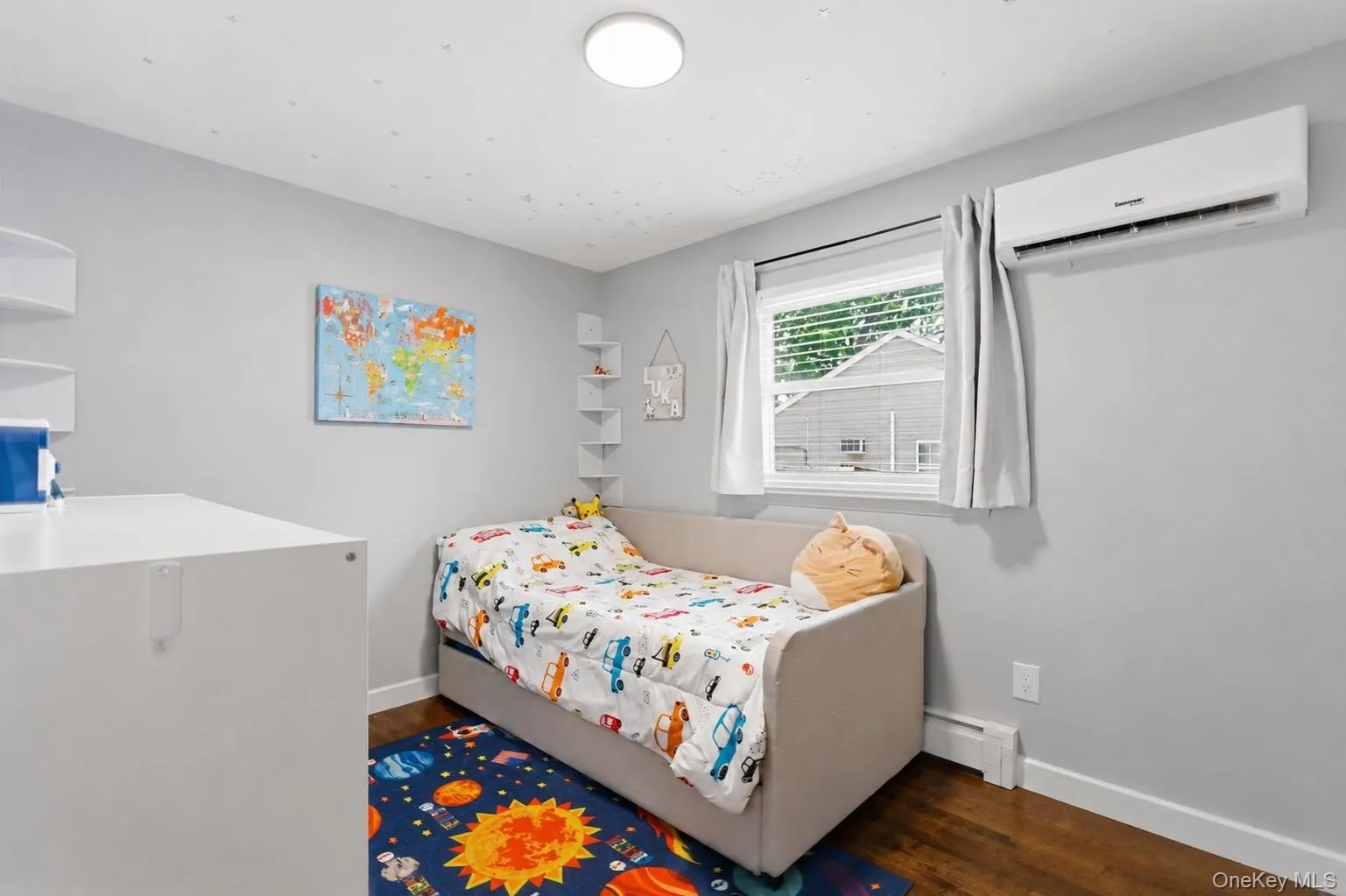 Bright room featuring a window with natural light, light gray walls, dark wood-finish flooring, a wall-mounted mini-split unit, and a flush-mount ceiling light fixture Bright room featuring a window with natural light, light gray walls, dark wood-finish flooring, a wall-mounted mini-split unit, and a flush-mount ceiling light fixture