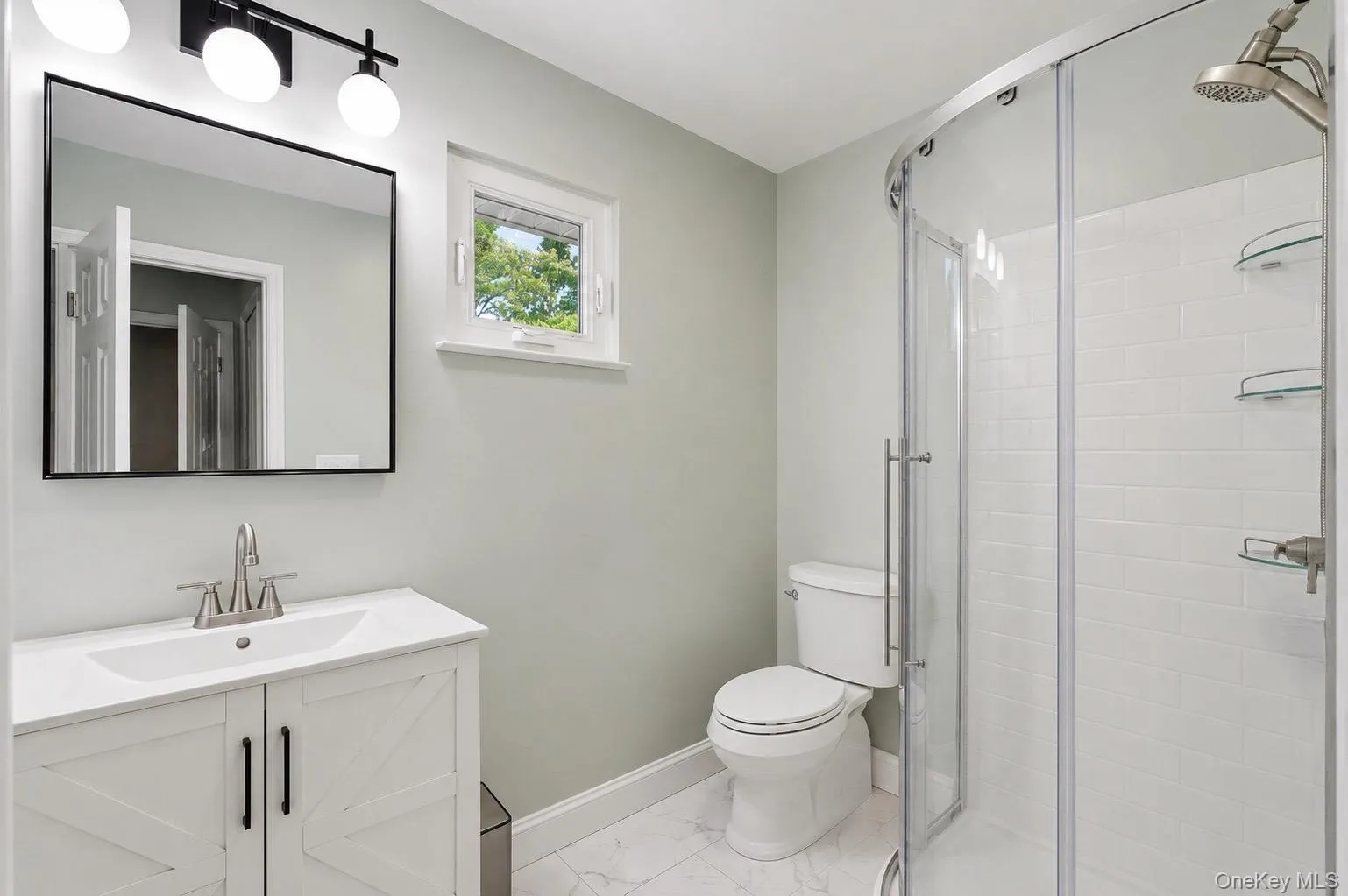 Bathroom featuring a white vanity and a curved glass shower enclosure with subway tile surround and built-in shelving Bathroom featuring a white vanity and a curved glass shower enclosure with subway tile surround and built-in shelving