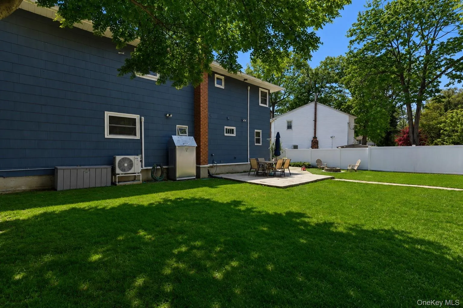 Spacious backyard featuring a large green lawn, a paver patio area, and a white vinyl fence Spacious backyard featuring a large green lawn, a paver patio area, and a white vinyl fence