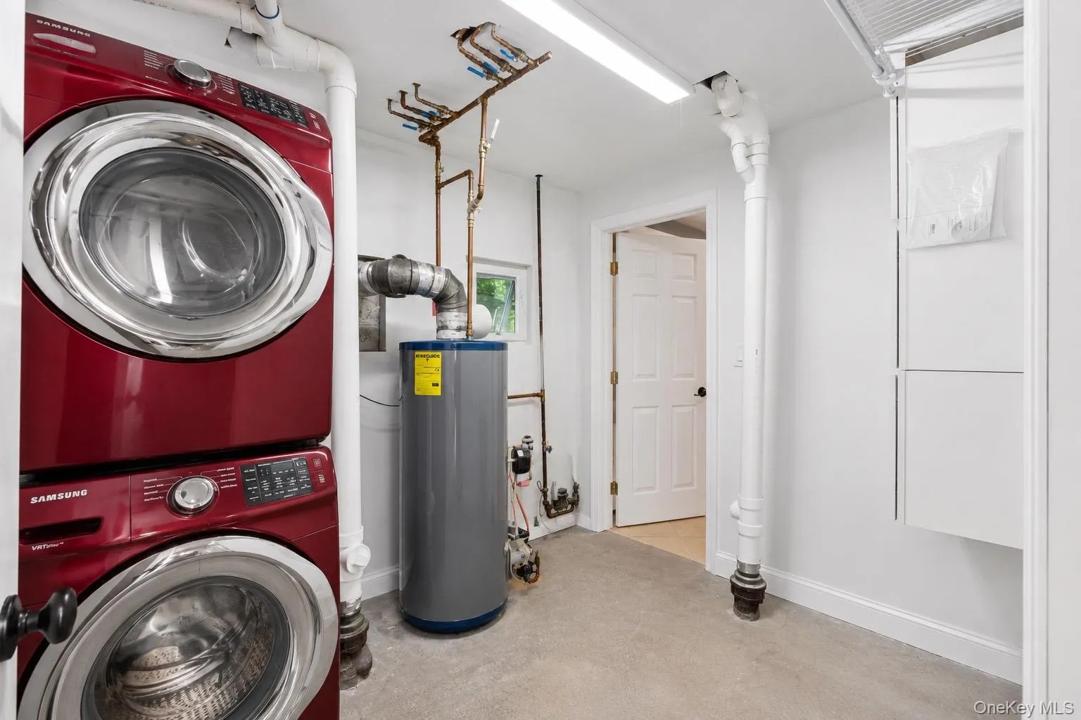 Dedicated utility area featuring a stacked washer and dryer, water heater, and built-in white cabinetry Dedicated utility area featuring a stacked washer and dryer, water heater, and built-in white cabinetry