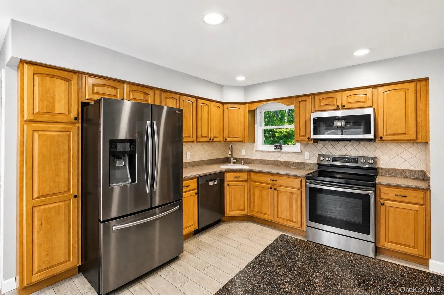 Kitchen featuring light wood cabinetry, stainless steel appliances, and a diagonal tile backsplash Kitchen featuring light wood cabinetry, stainless steel appliances, and a diagonal tile backsplash