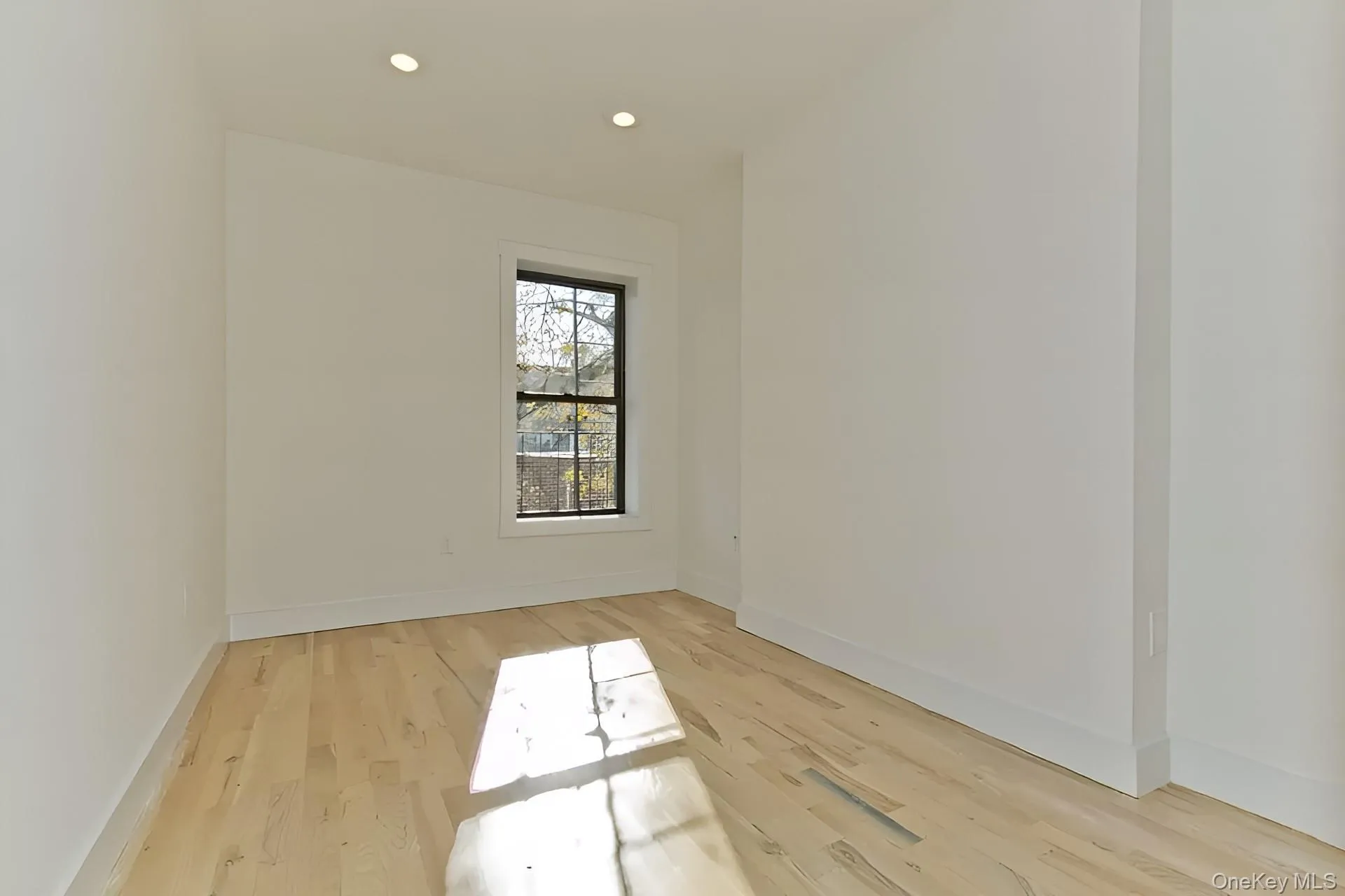 Bright room featuring light wood-finish flooring, recessed lighting, and a single window with dark framing Bright room featuring light wood-finish flooring, recessed lighting, and a single window with dark framing