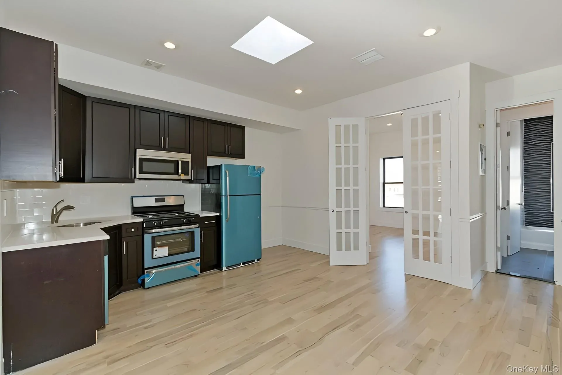 Kitchen featuring dark cabinetry, stainless steel appliances, a white tile backsplash, and light wood-finish flooring Kitchen featuring dark cabinetry, stainless steel appliances, a white tile backsplash, and light wood-finish flooring