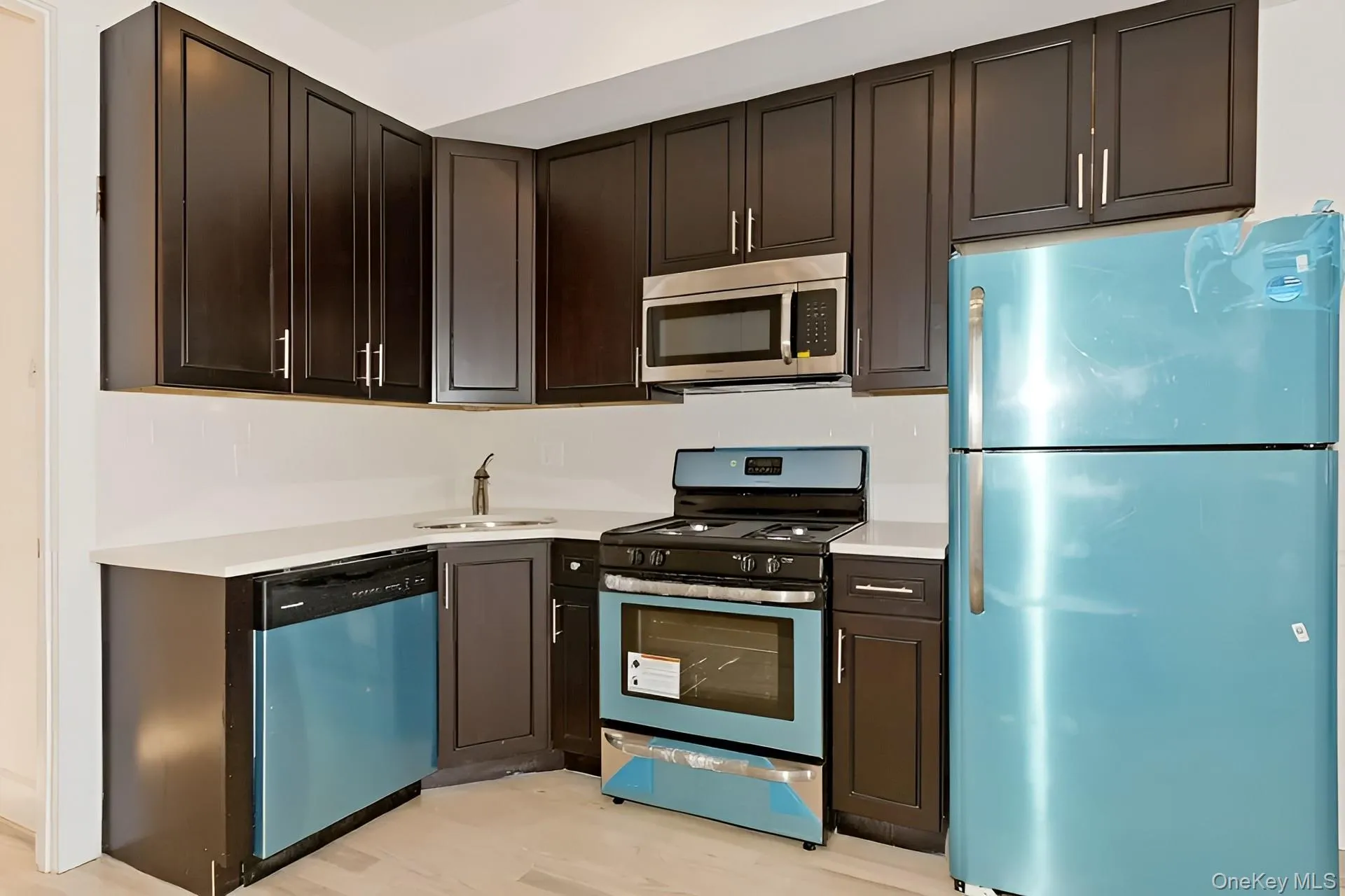 Kitchen featuring dark wood cabinetry, white countertops, stainless steel microwave, gas range, and a corner sink Kitchen featuring dark wood cabinetry, white countertops, stainless steel microwave, gas range, and a corner sink