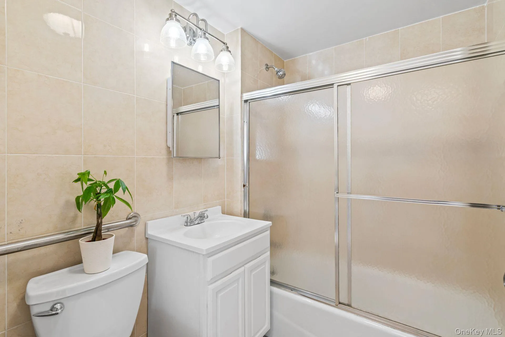 Full bathroom featuring vanity, toilet, combined bath / shower with glass door, and tile walls Full bathroom featuring vanity, toilet, combined bath / shower with glass door, and tile walls