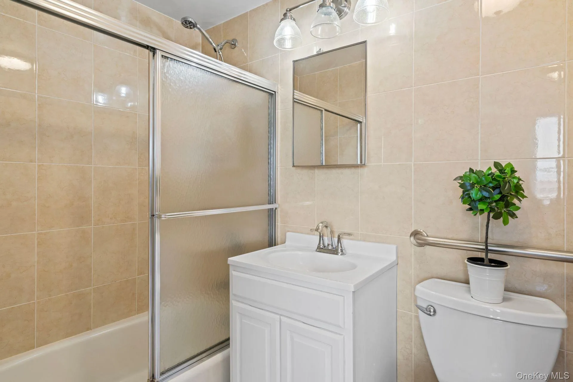 Full bathroom with toilet, vanity, shower / bath combination with glass door, and tile walls Full bathroom with toilet, vanity, shower / bath combination with glass door, and tile walls