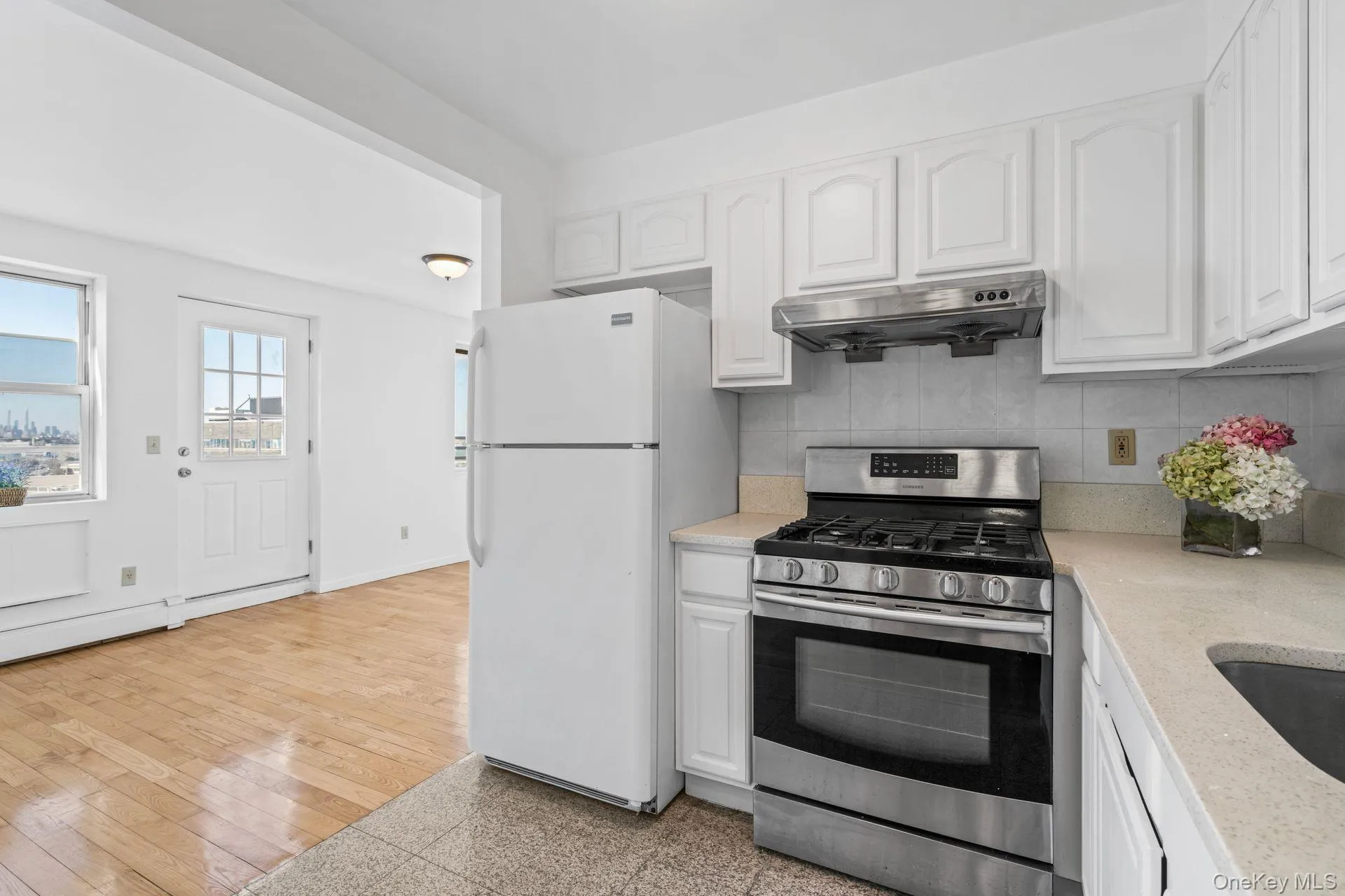 Kitchen featuring tasteful backsplash, white cabinetry, white refrigerator, gas range, and light hardwood / wood-style flooring Kitchen featuring tasteful backsplash, white cabinetry, white refrigerator, gas range, and light hardwood / wood-style flooring