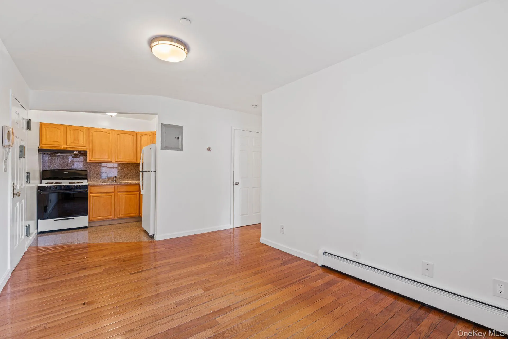 Kitchen with light brown cabinetry, light wood-type flooring, baseboard heating, white appliances, and decorative backsplash Kitchen with light brown cabinetry, light wood-type flooring, baseboard heating, white appliances, and decorative backsplash