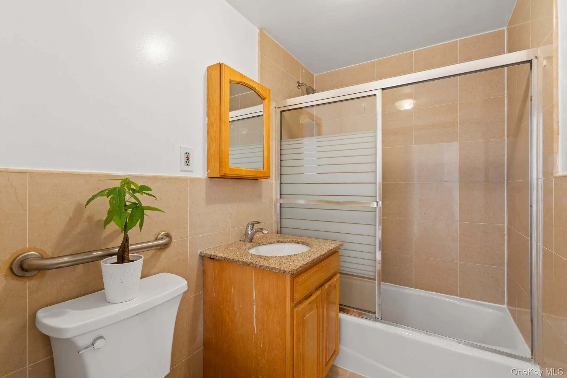 Full bathroom featuring vanity, tile walls, shower / bath combination with glass door, and toilet Full bathroom featuring vanity, tile walls, shower / bath combination with glass door, and toilet
