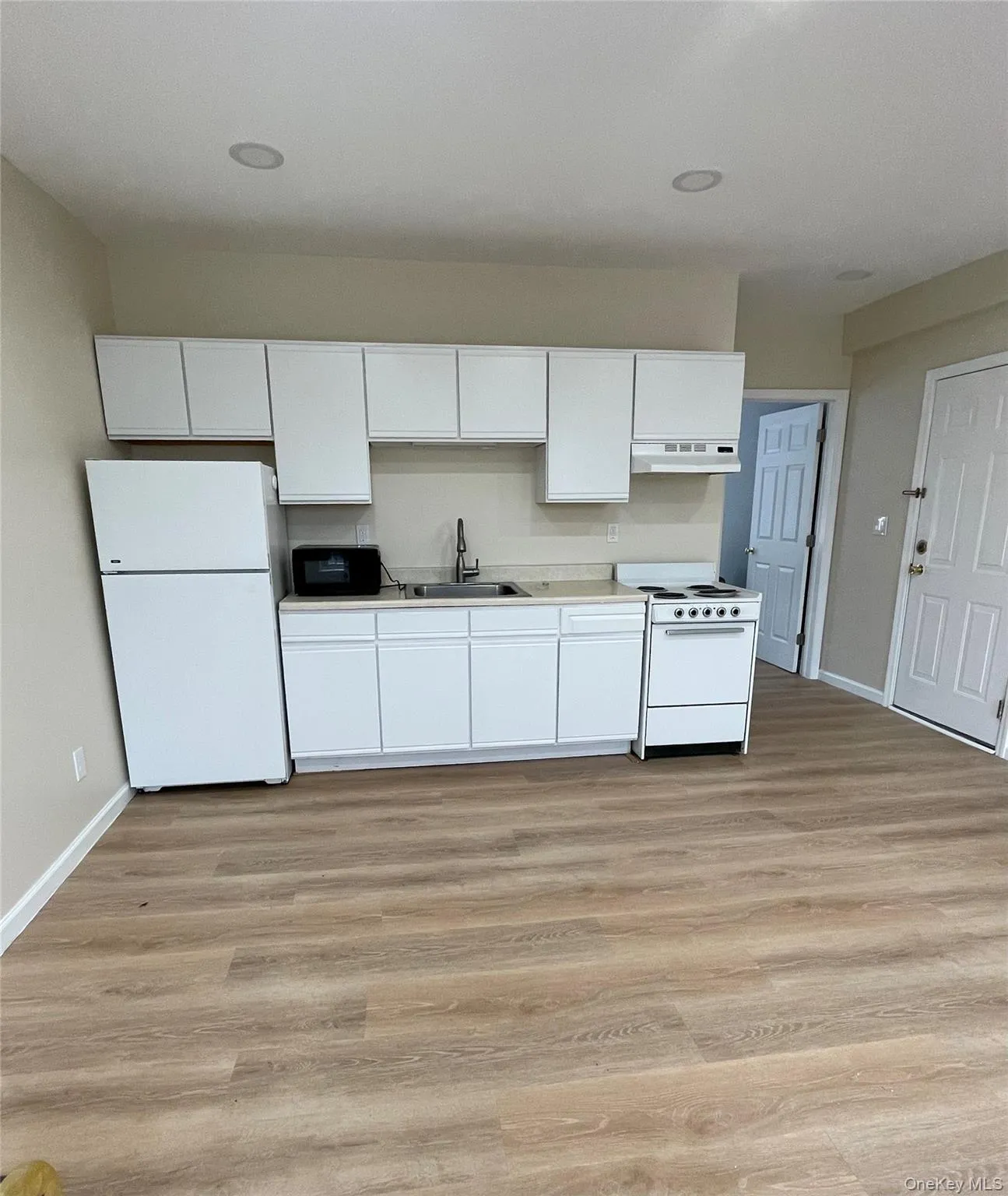 Kitchen featuring sink, range hood, white appliances, white cabinets, and light wood-type flooring Kitchen featuring sink, range hood, white appliances, white cabinets, and light wood-type flooring
