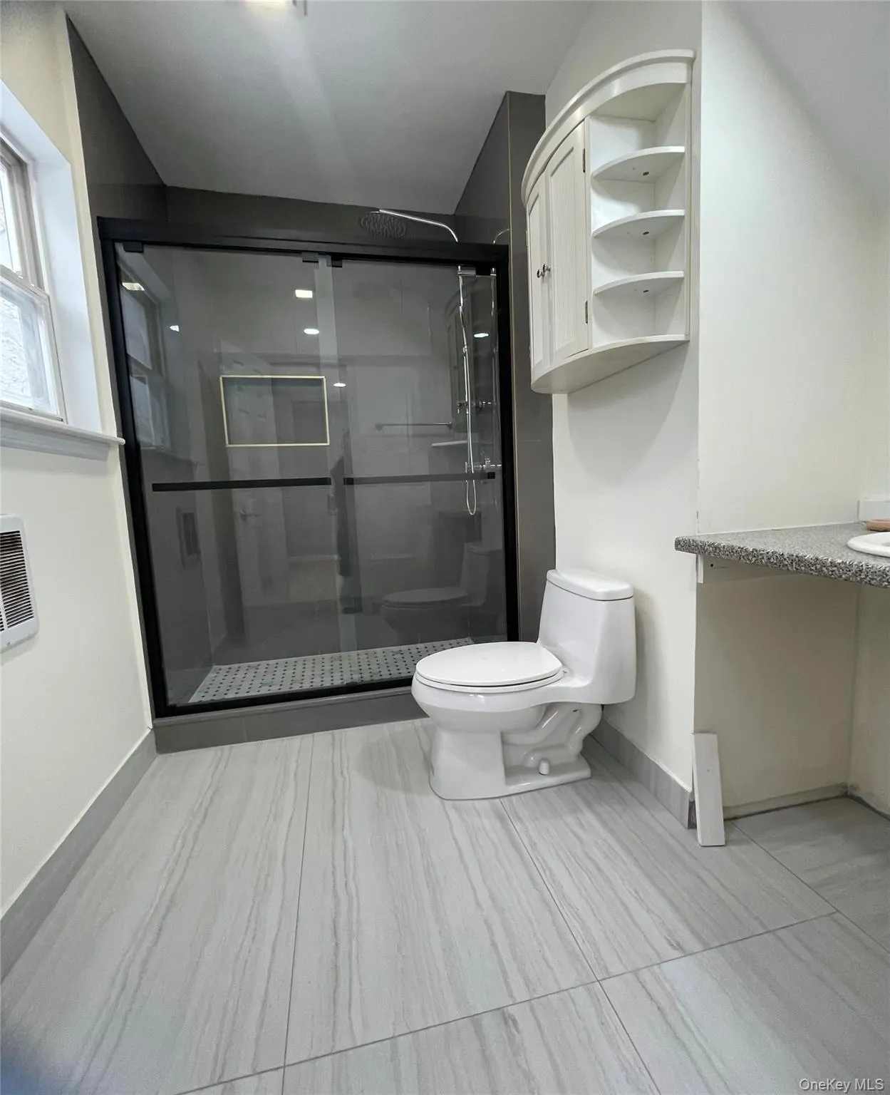 Bathroom featuring vanity, heating unit, toilet, and a shower with shower door Bathroom featuring vanity, heating unit, toilet, and a shower with shower door