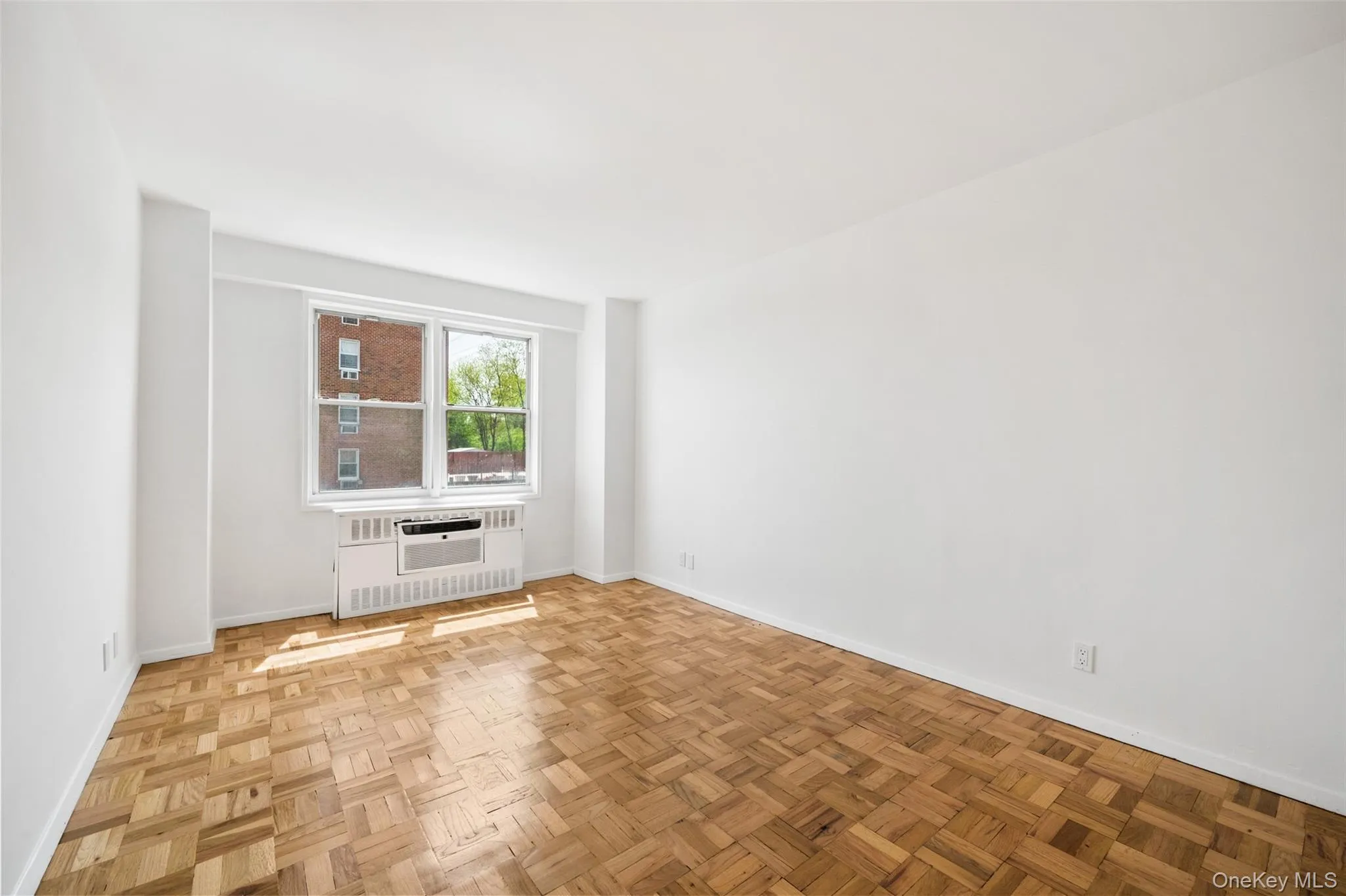 2nd Bedroom, South west facing. Parquet wood flooring throughout a room with white painted walls and a window featuring a window-mounted air conditioning unit 2nd Bedroom, South west facing. Parquet wood flooring throughout a room with white painted walls and a window featuring a window-mounted air conditioning unit