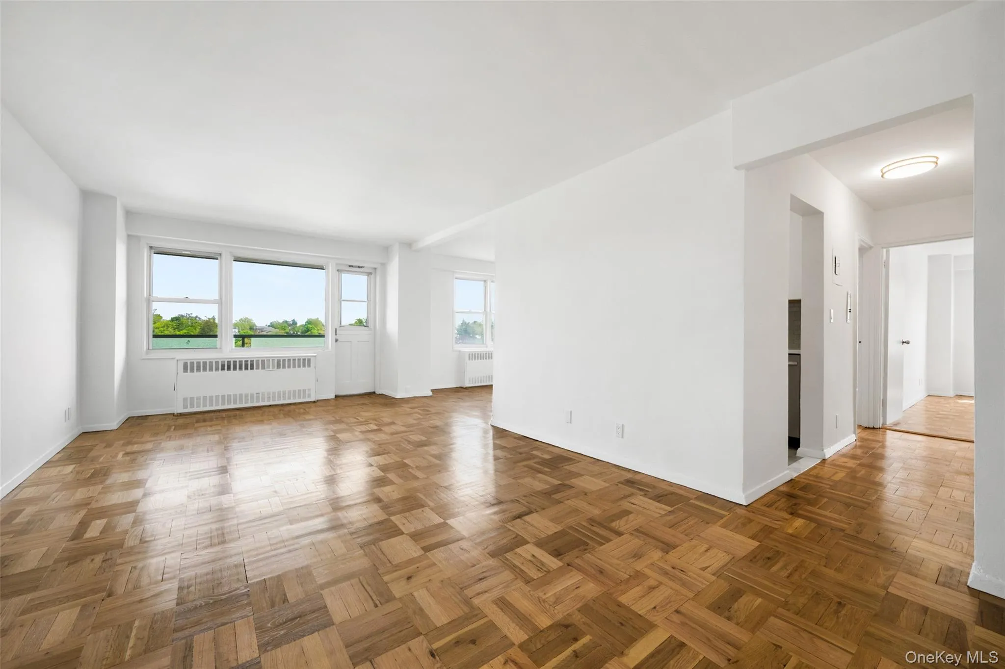 Spacious interior featuring parquet wood flooring, multiple windows, a white radiator, and an entry alcove Spacious interior featuring parquet wood flooring, multiple windows, a white radiator, and an entry alcove