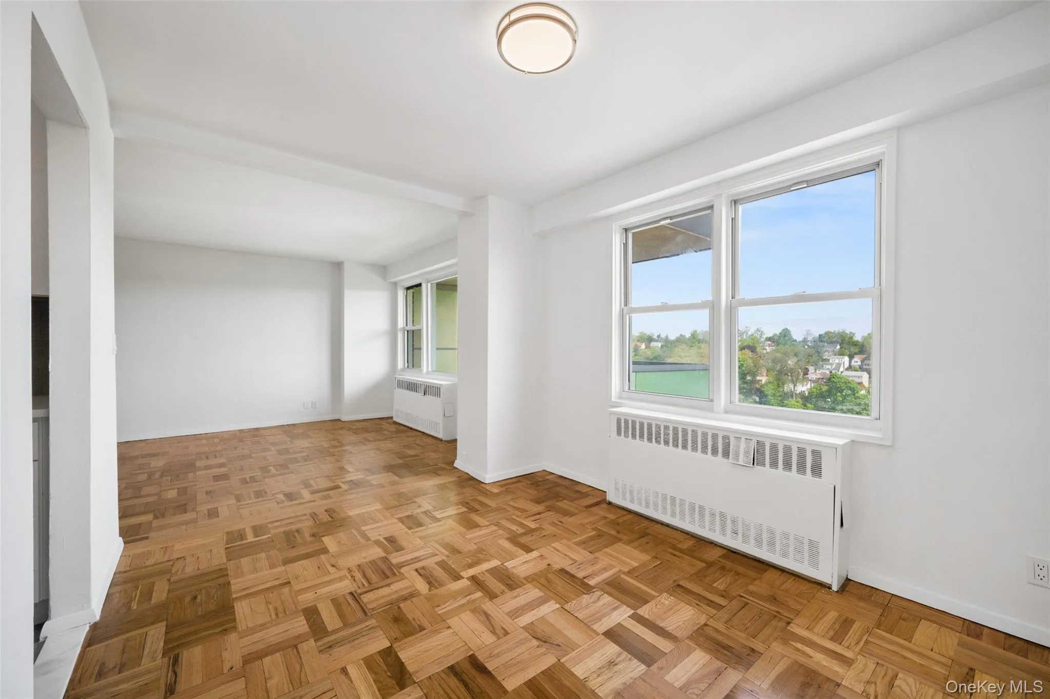 Spacious interior featuring parquet wood flooring, white walls, and a contemporary ceiling light fixture Spacious interior featuring parquet wood flooring, white walls, and a contemporary ceiling light fixture