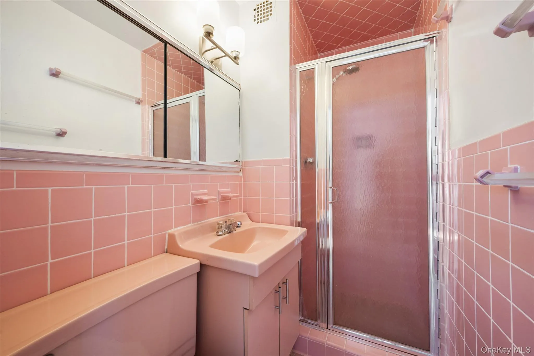 Bathroom featuring pink square wall tiling, a matching pink vanity with integrated sink, and a shower enclosure with a frosted glass door Bathroom featuring pink square wall tiling, a matching pink vanity with integrated sink, and a shower enclosure with a frosted glass door