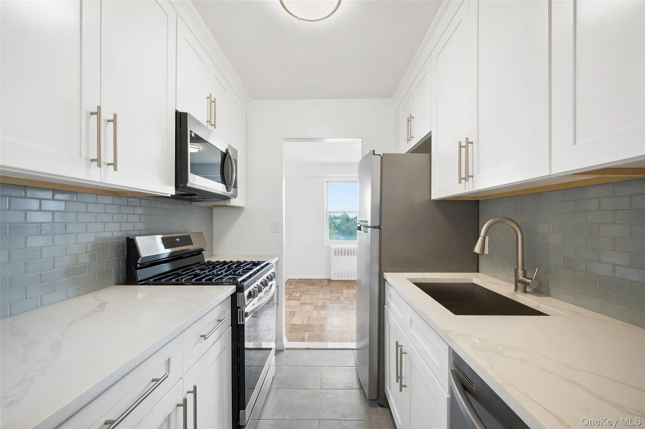 Galley of brand new kitchen featuring white shaker cabinetry, stainless steel appliances, a light-toned countertop, and a subway tile backsplash Galley of brand new kitchen featuring white shaker cabinetry, stainless steel appliances, a light-toned countertop, and a subway tile backsplash