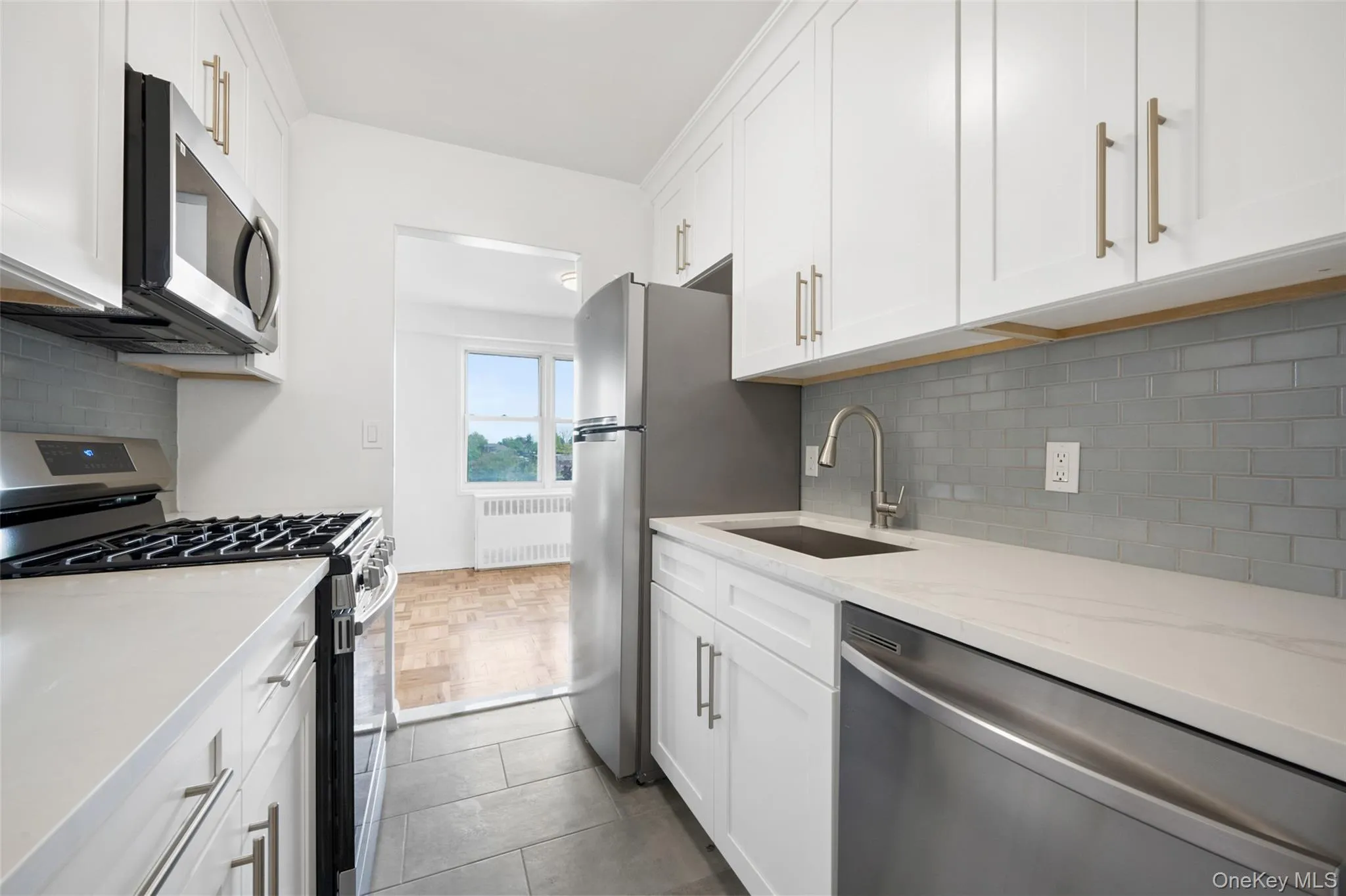 Brand New Fully renovated kitchen featuring white shaker-style cabinetry with gold-toned hardware, white solid surface countertops, and a full suite of stainless steel appliances Brand New Fully renovated kitchen featuring white shaker-style cabinetry with gold-toned hardware, white solid surface countertops, and a full suite of stainless steel appliances