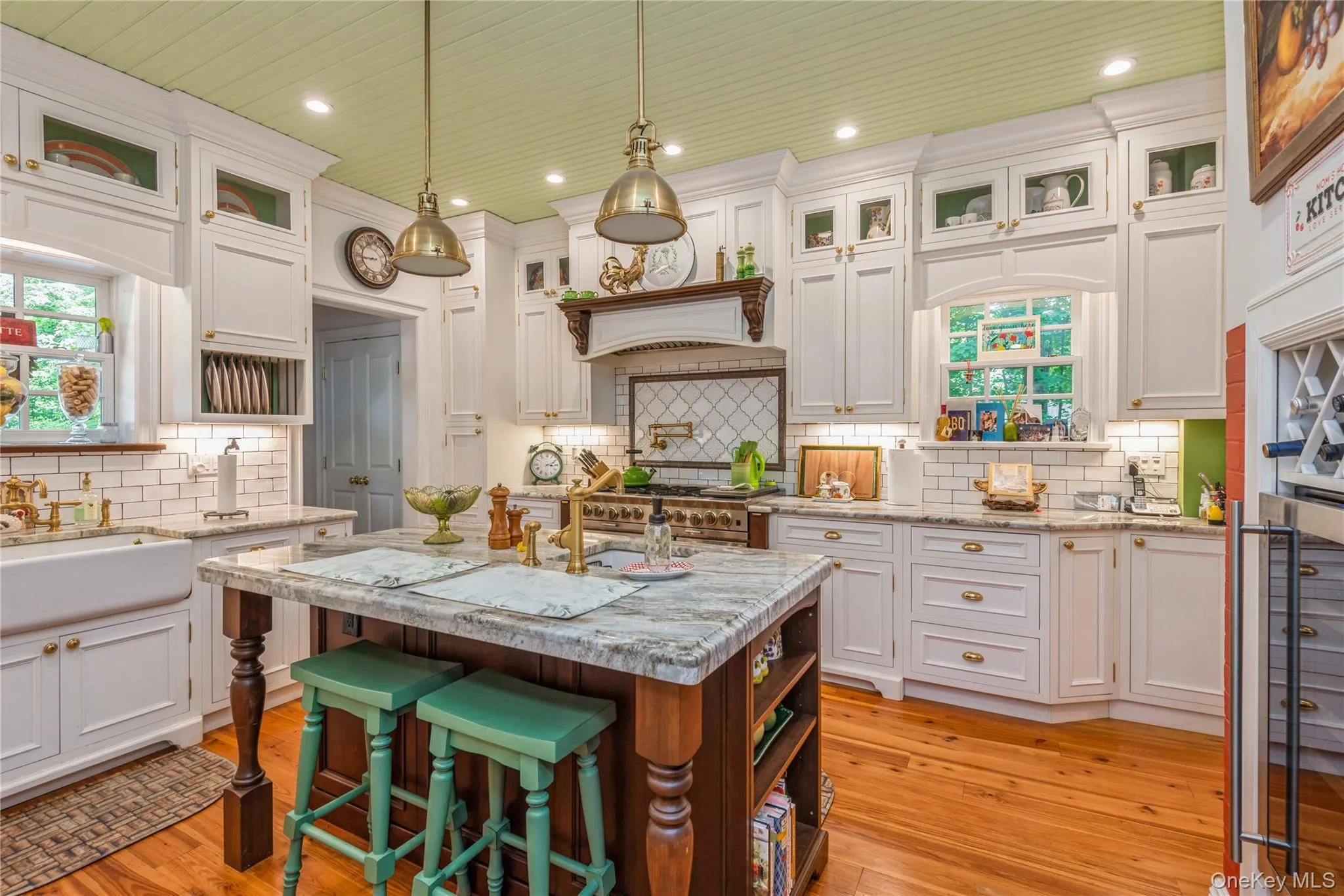 Gourmet kitchen featuring a central island with granite countertop, white shaker cabinetry with brass hardware, subway tile backsplash, and wood-finish flooring Gourmet kitchen featuring a central island with granite countertop, white shaker cabinetry with brass hardware, subway tile backsplash, and wood-finish flooring