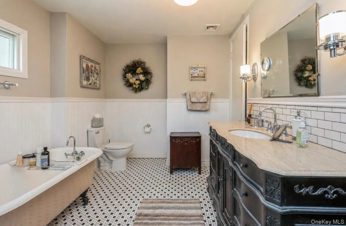 Bathroom featuring a clawfoot bathtub, black and white hexagonal tile flooring, a double vanity and beadboard paneling Bathroom featuring a clawfoot bathtub, black and white hexagonal tile flooring, a double vanity and beadboard paneling