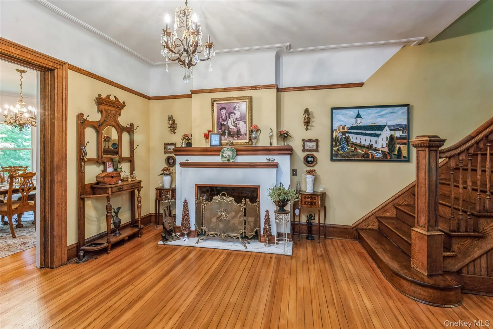 Spacious entry hall featuring wood-finish flooring, a decorative fireplace with a mantel, a chandelier, and an intricately carved wooden staircase Spacious entry hall featuring wood-finish flooring, a decorative fireplace with a mantel, a chandelier, and an intricately carved wooden staircase