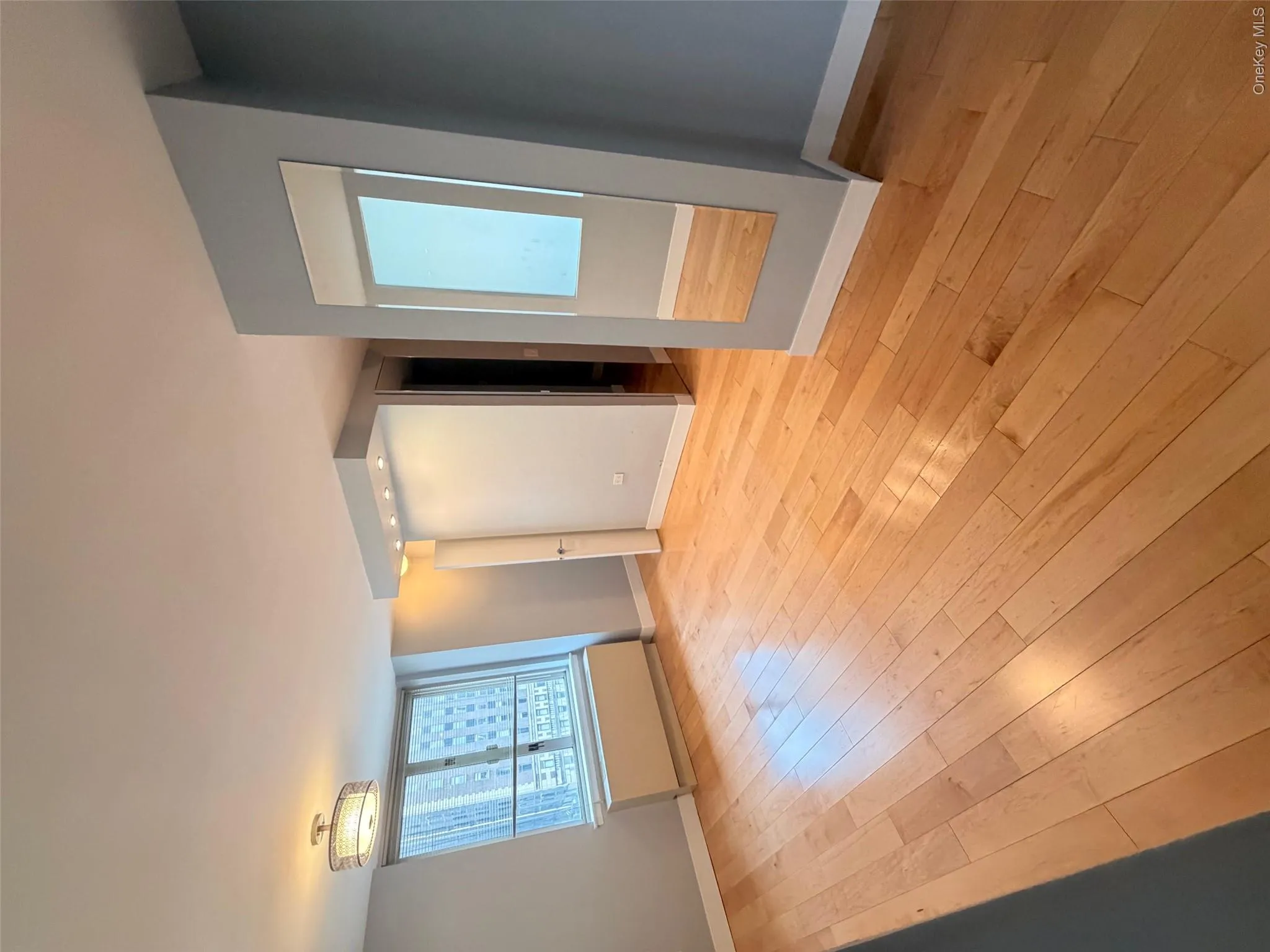 Hardwood flooring throughout, featuring a window with city buildings visible, a ceiling-mounted light fixture, recessed lighting, and a full-length wall mirror Hardwood flooring throughout, featuring a window with city buildings visible, a ceiling-mounted light fixture, recessed lighting, and a full-length wall mirror