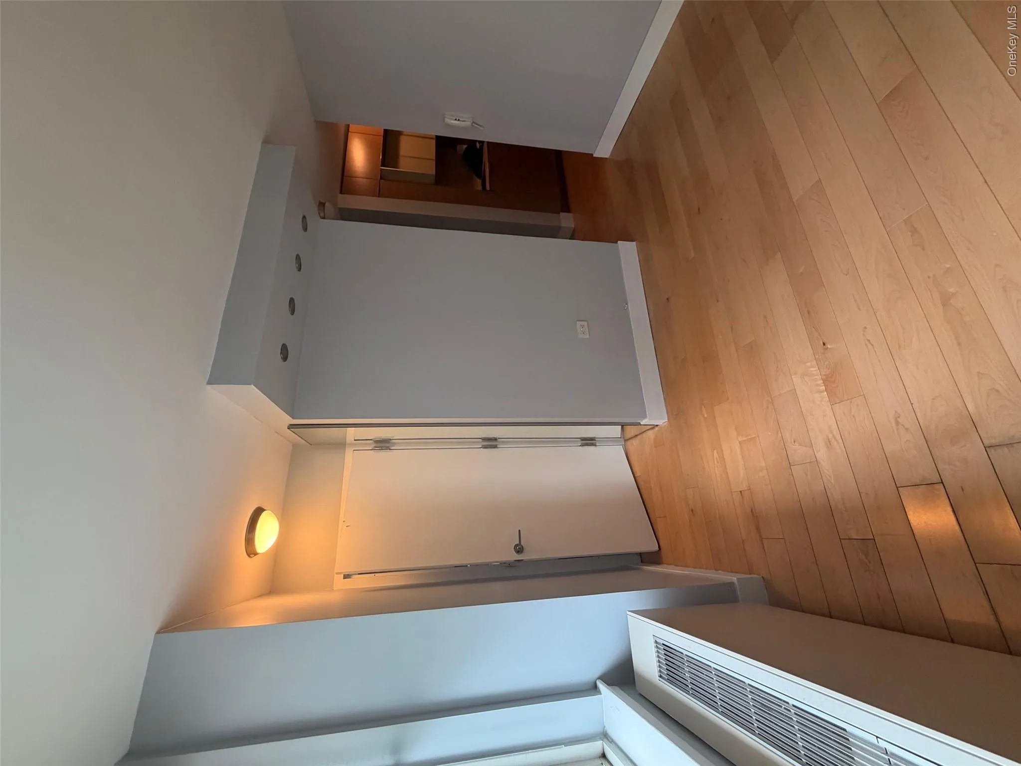 Hardwood flooring throughout, featuring a window with city buildings visible, a ceiling-mounted light fixture, recessed lighting, and a full-length wall mirror Hardwood flooring throughout, featuring a window with city buildings visible, a ceiling-mounted light fixture, recessed lighting, and a full-length wall mirror