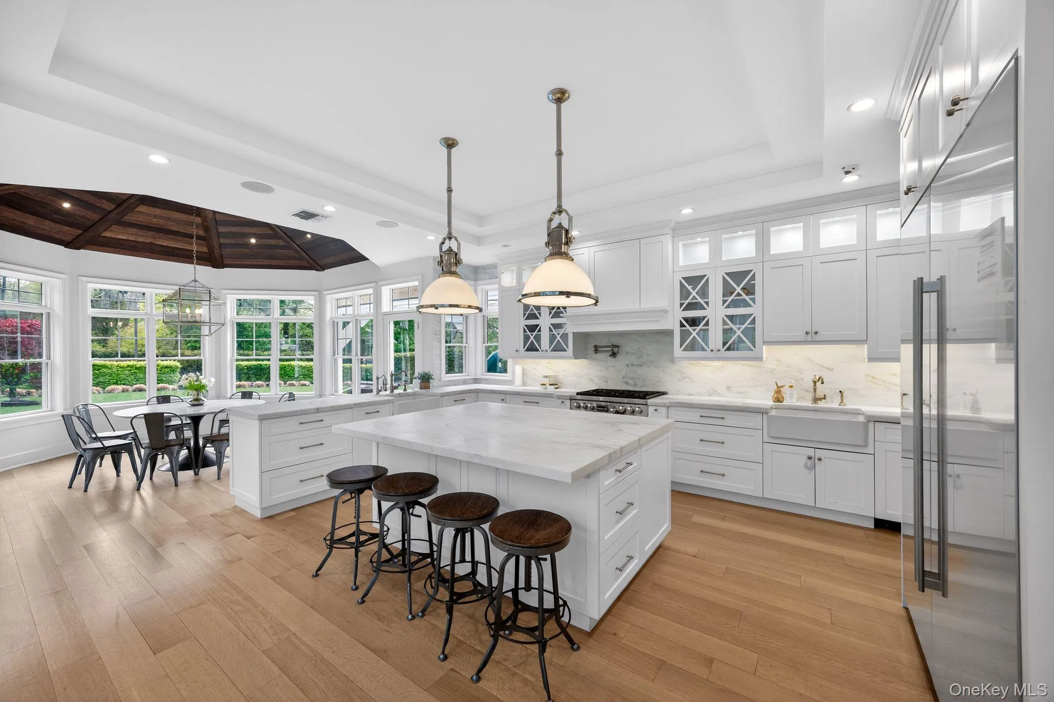 Gourmet kitchen featuring a large central island with seating, white shaker cabinetry, stone countertops, and wood-finish flooring Gourmet kitchen featuring a large central island with seating, white shaker cabinetry, stone countertops, and wood-finish flooring