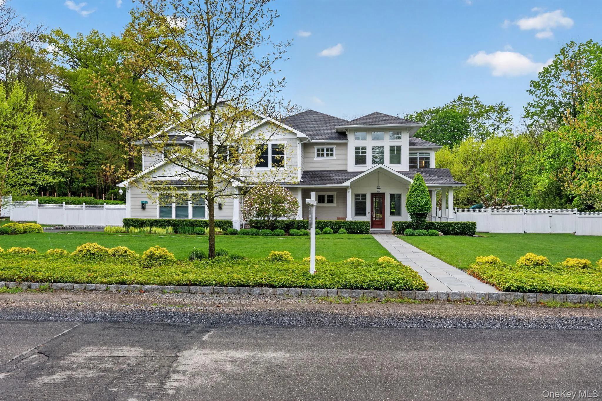Expansive front lawn bordered by mature trees and a white privacy fence Expansive front lawn bordered by mature trees and a white privacy fence