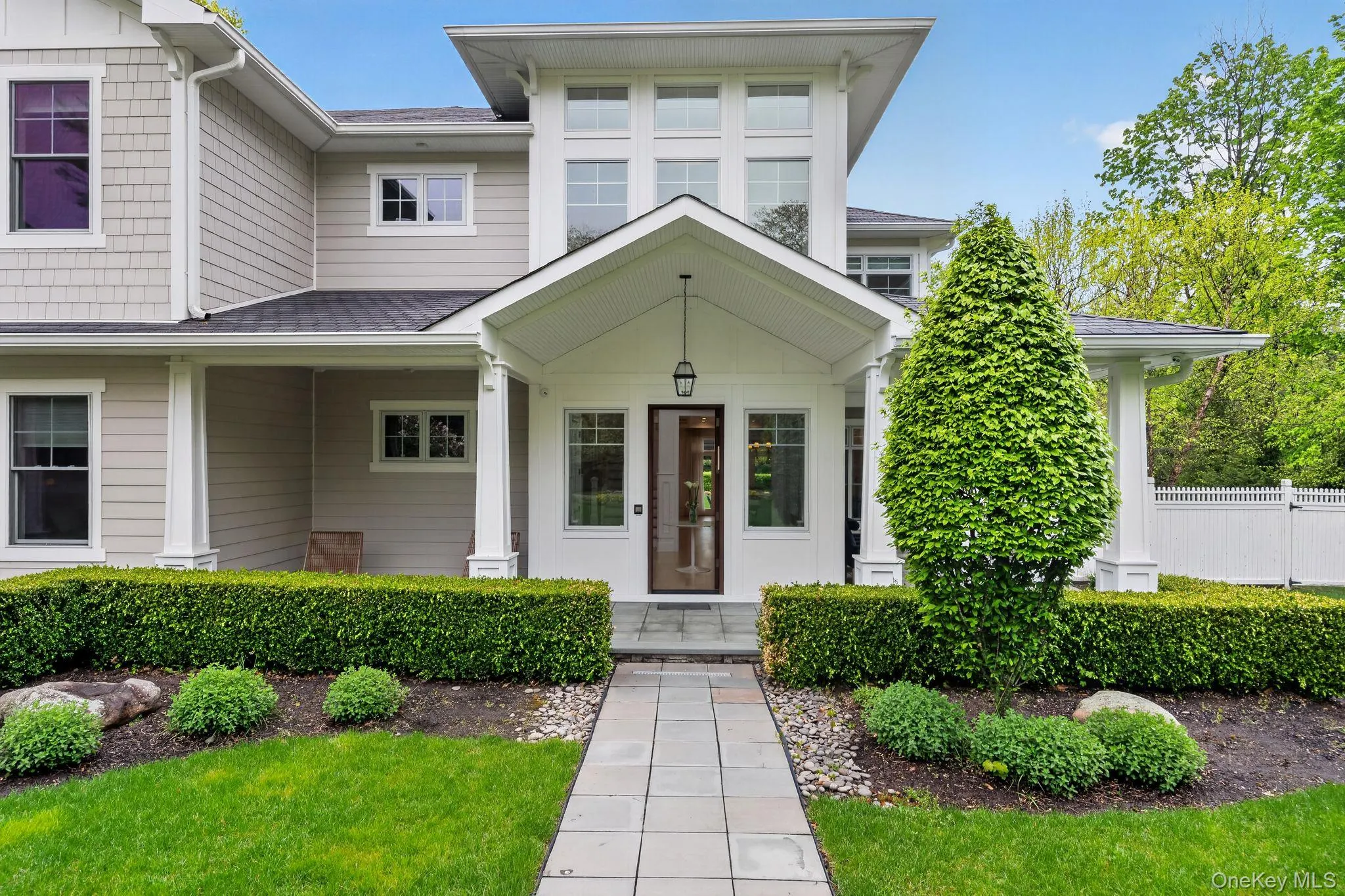 Modern exterior featuring a prominent covered entryway, shaker siding, and a stone-paver walkway Modern exterior featuring a prominent covered entryway, shaker siding, and a stone-paver walkway