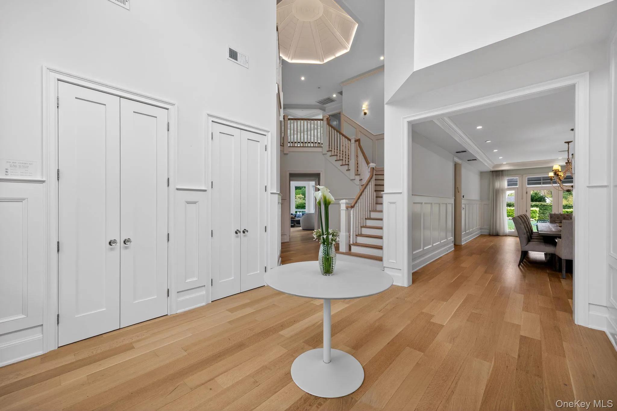 Foyer showcasing light wood-finish flooring, white paneled walls, and a grand staircase with wood railings Foyer showcasing light wood-finish flooring, white paneled walls, and a grand staircase with wood railings