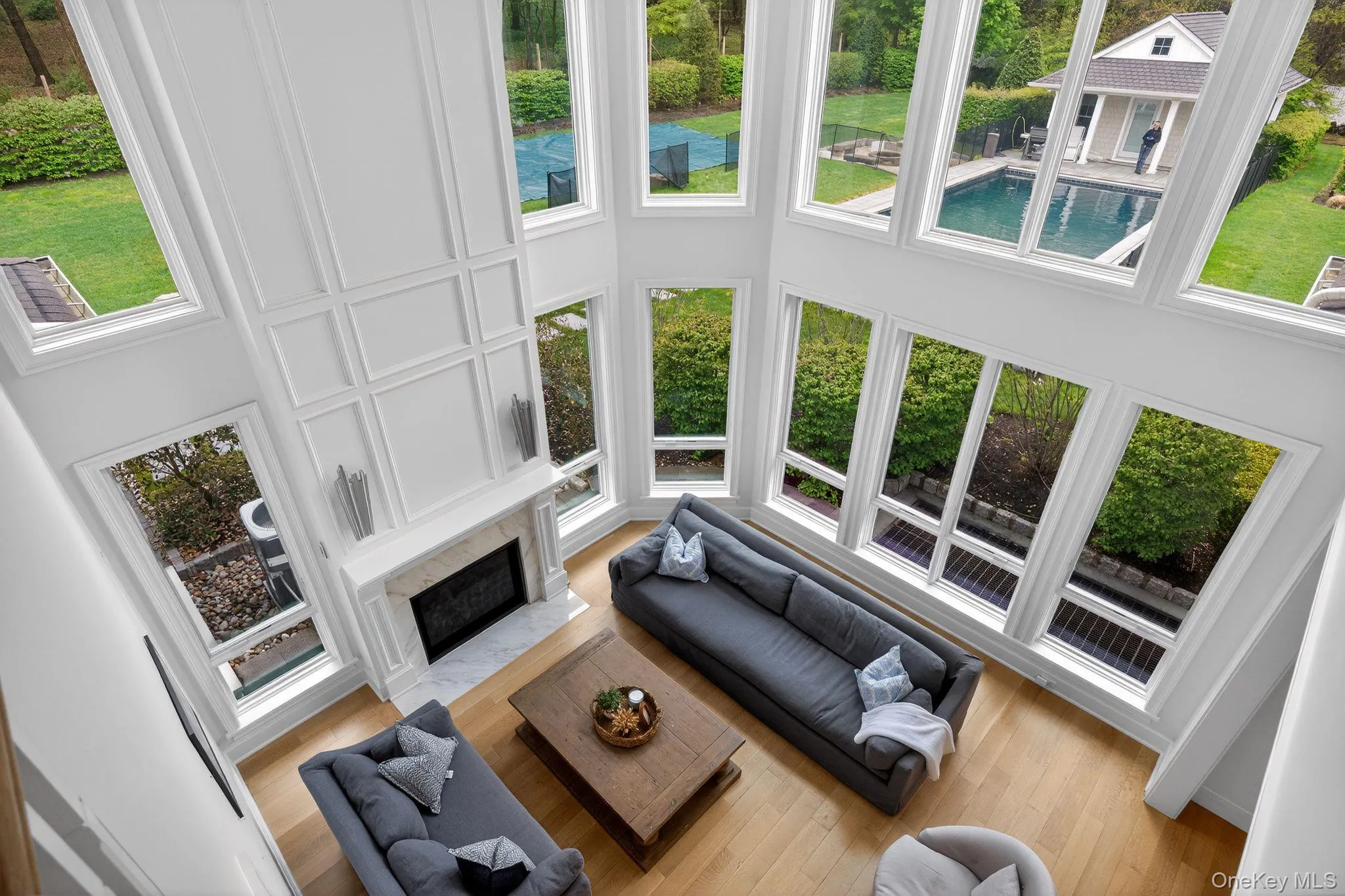Two-story living area featuring a fireplace with stone mantel, extensive wall paneling, and wood-finish flooring Two-story living area featuring a fireplace with stone mantel, extensive wall paneling, and wood-finish flooring