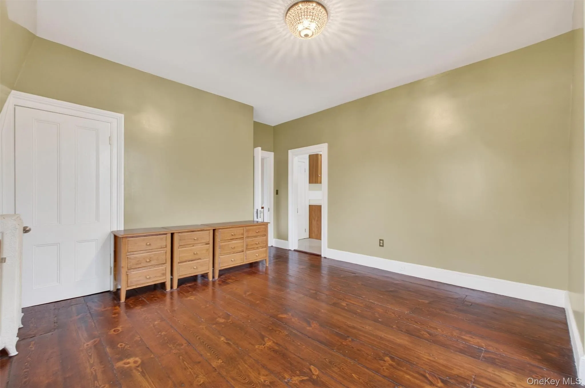 Room featuring wide plank hardwood flooring, two large double-hung windows, and a ceiling-mounted light fixture. Room featuring wide plank hardwood flooring, two large double-hung windows, and a ceiling-mounted light fixture.