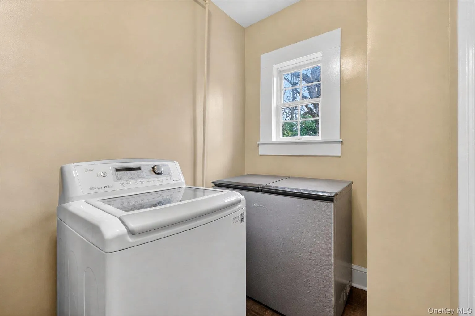 Laundry area featuring a large window with white trim, tan painted walls, and hardwood flooring Laundry area featuring a large window with white trim, tan painted walls, and hardwood flooring