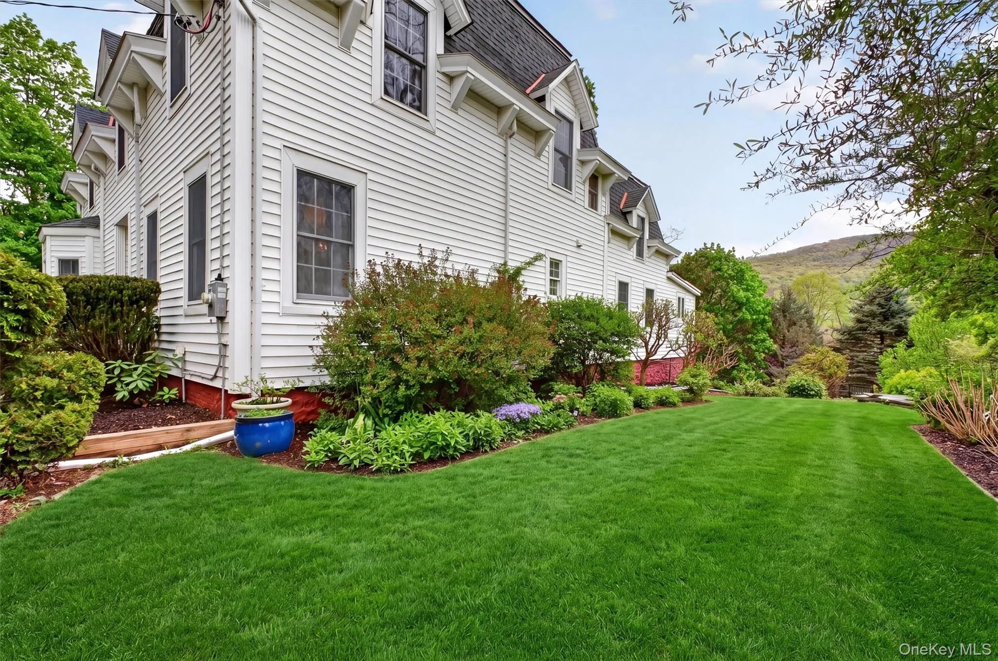 Expansive green lawn framed by manicured hedges, mature trees, and plants, leading to the backyard with views of the hills and mountain. Expansive green lawn framed by manicured hedges, mature trees, and plants, leading to the backyard with views of the hills and mountain.