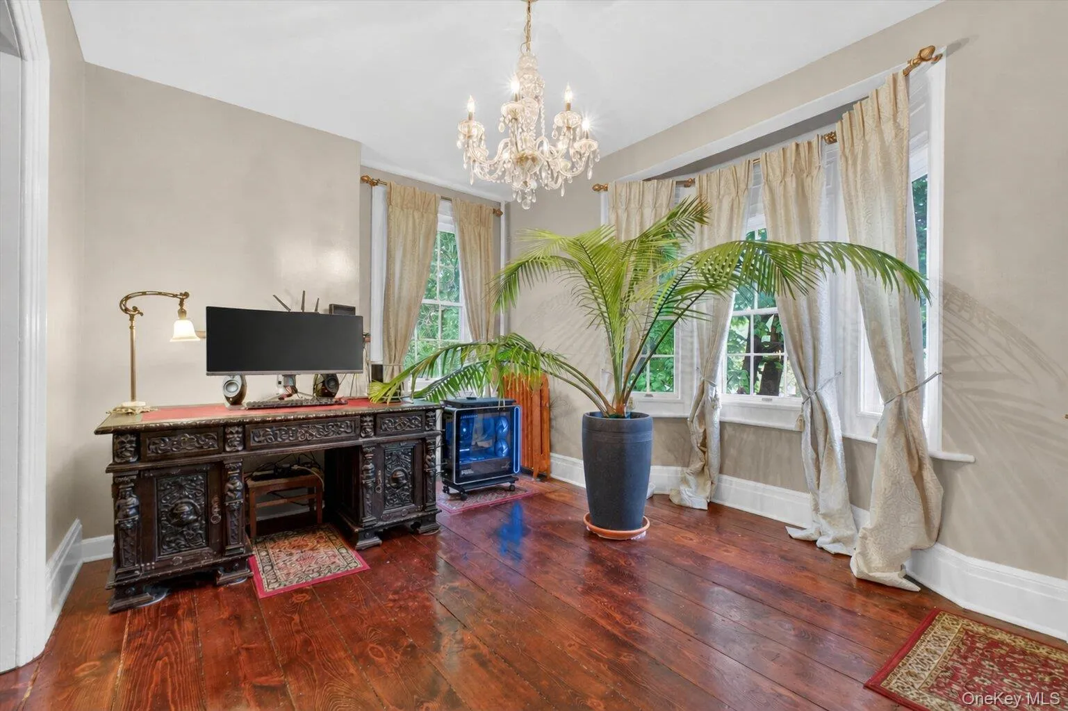 Hardwood flooring extending through an arched doorway, featuring a crystal chandelier and large bay windows. Hardwood flooring extending through an arched doorway, featuring a crystal chandelier and large bay windows.