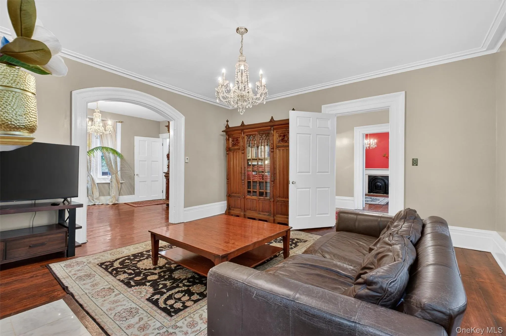 Living area featuring crystal chandelier, hardwood floors, a decorative fireplace with a mantel, arched doorways leading to other living areas, and white trim molding Living area featuring crystal chandelier, hardwood floors, a decorative fireplace with a mantel, arched doorways leading to other living areas, and white trim molding