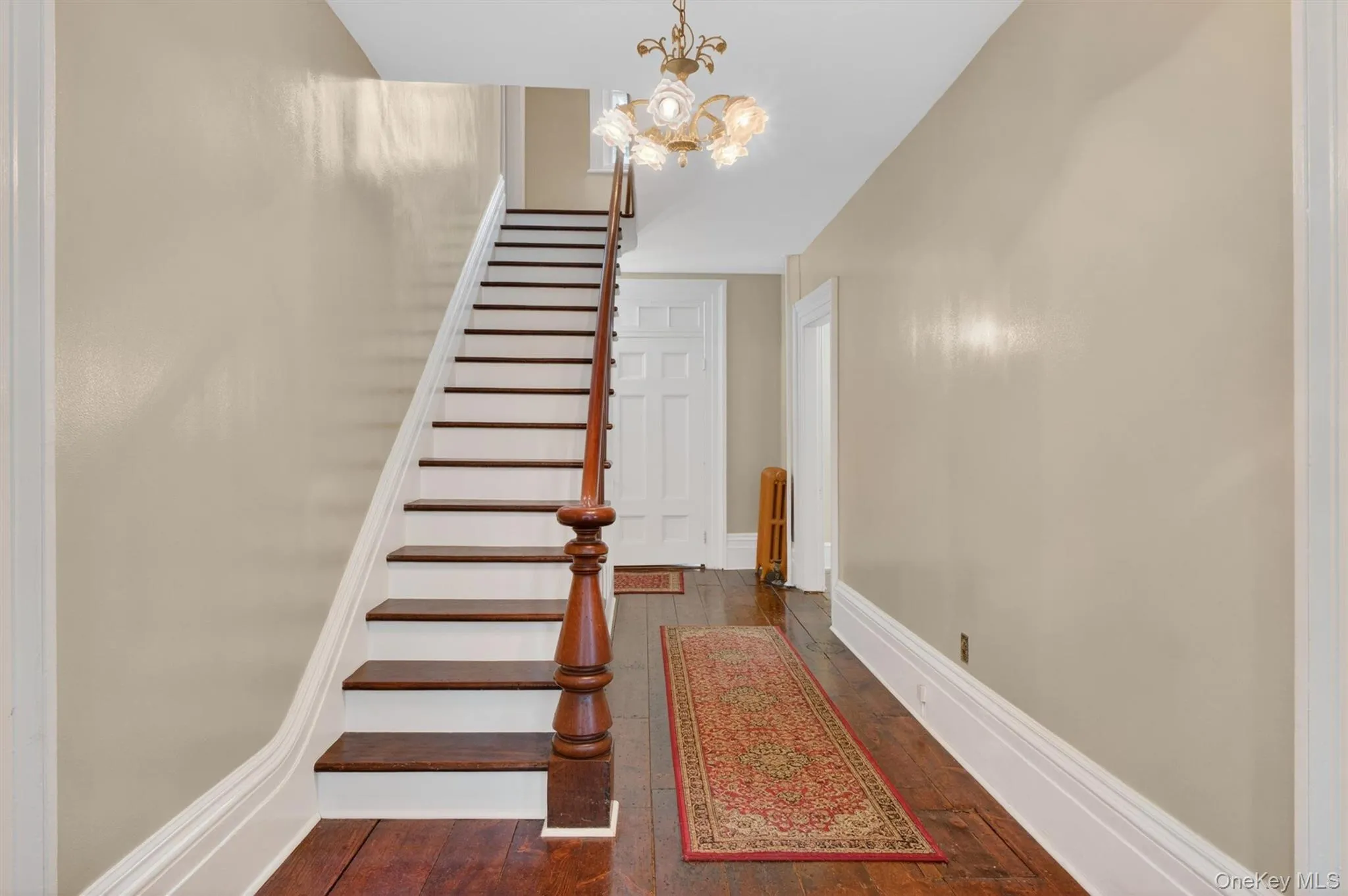 Foyer showcasing hardwood flooring, a classic chandelier, a dark wood staircase with balusters, and hallway leading into other areas. Foyer showcasing hardwood flooring, a classic chandelier, a dark wood staircase with balusters, and hallway leading into other areas.