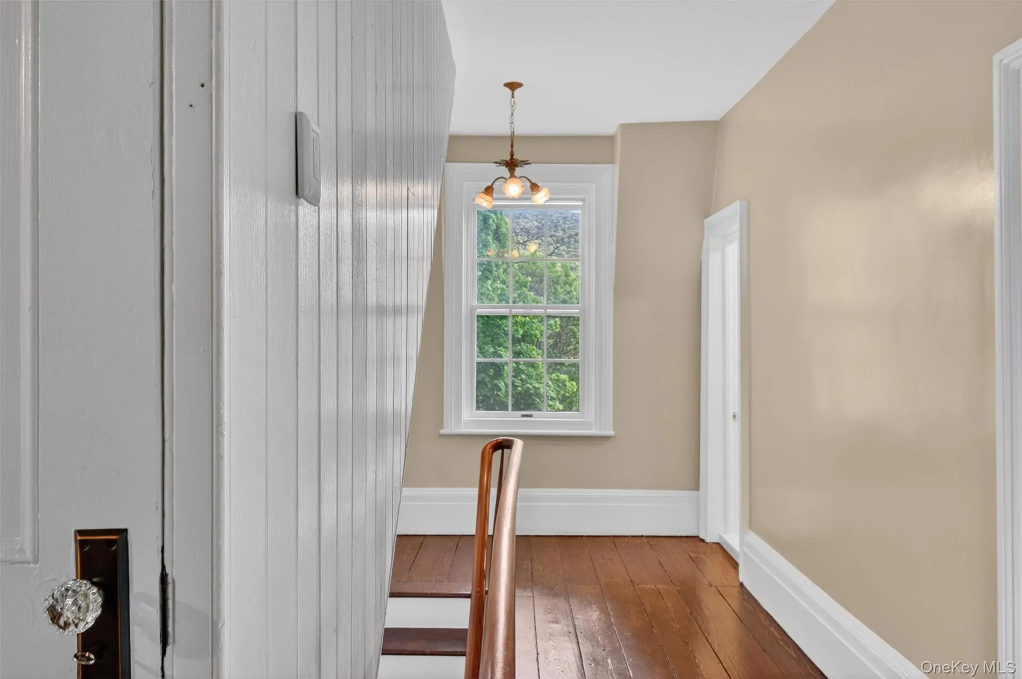 Second-story hallway featuring rich hardwood flooring, antique lighting fixture, a classic wooden balustrade, and doors leading to other living areas. Second-story hallway featuring rich hardwood flooring, antique lighting fixture, a classic wooden balustrade, and doors leading to other living areas.