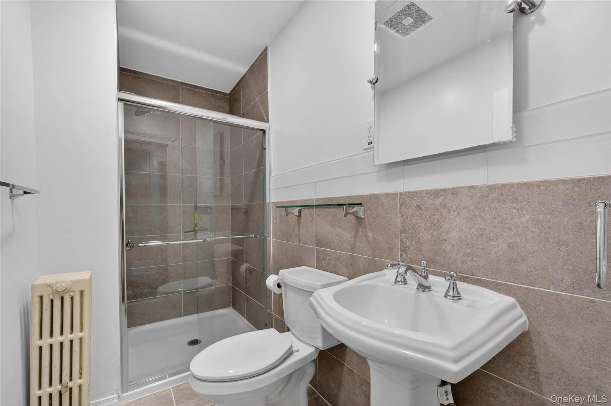Bathroom featuring a glass-enclosed shower, pedestal sink with chrome fixtures, tiled walls, and a recessed medicine cabinet mirror. Bathroom featuring a glass-enclosed shower, pedestal sink with chrome fixtures, tiled walls, and a recessed medicine cabinet mirror.