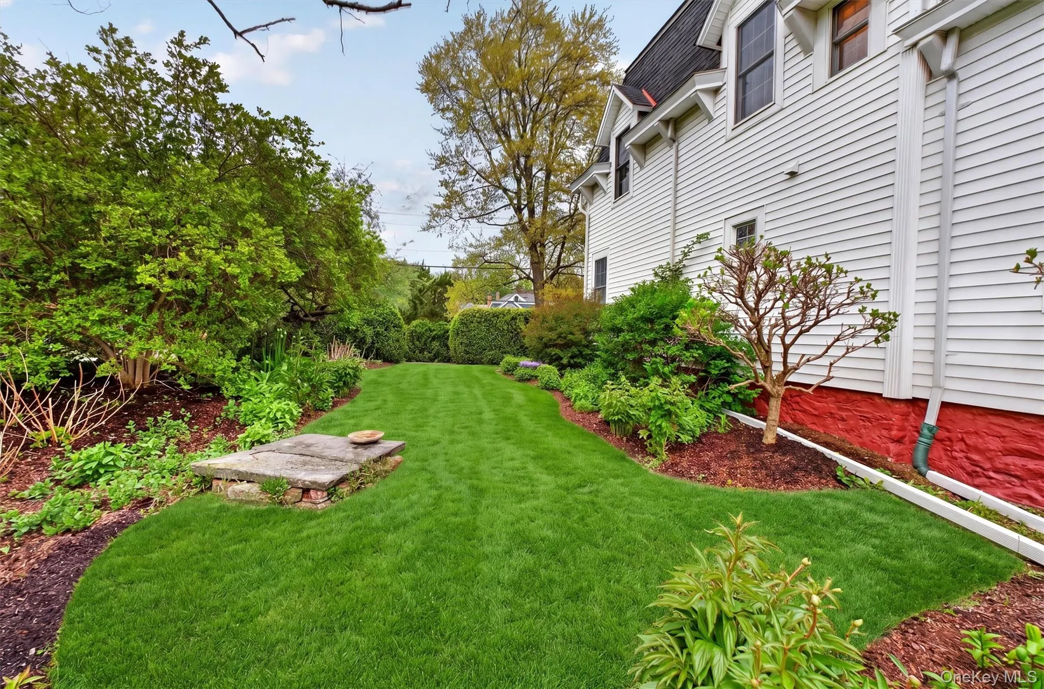 Expansive green lawn framed by manicured hedges, mature trees, and plants, leading to the backyard with views of the hills and mountain. Expansive green lawn framed by manicured hedges, mature trees, and plants, leading to the backyard with views of the hills and mountain.
