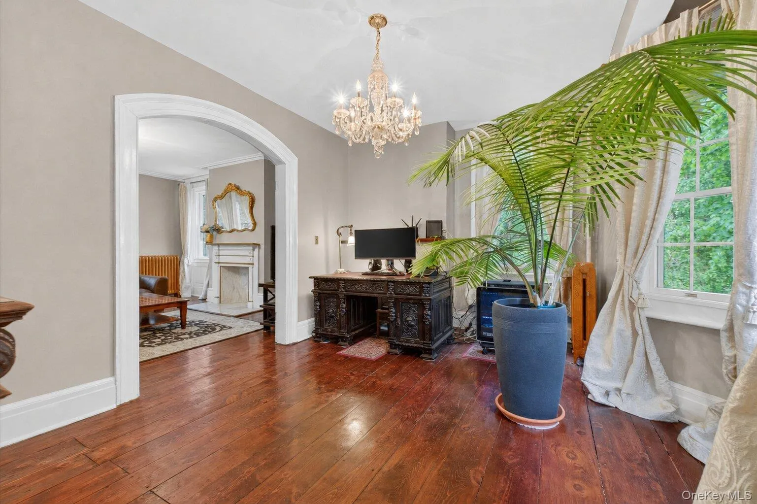 Hardwood flooring extending through an arched doorway, featuring a crystal chandelier and large bay windows. Hardwood flooring extending through an arched doorway, featuring a crystal chandelier and large bay windows.
