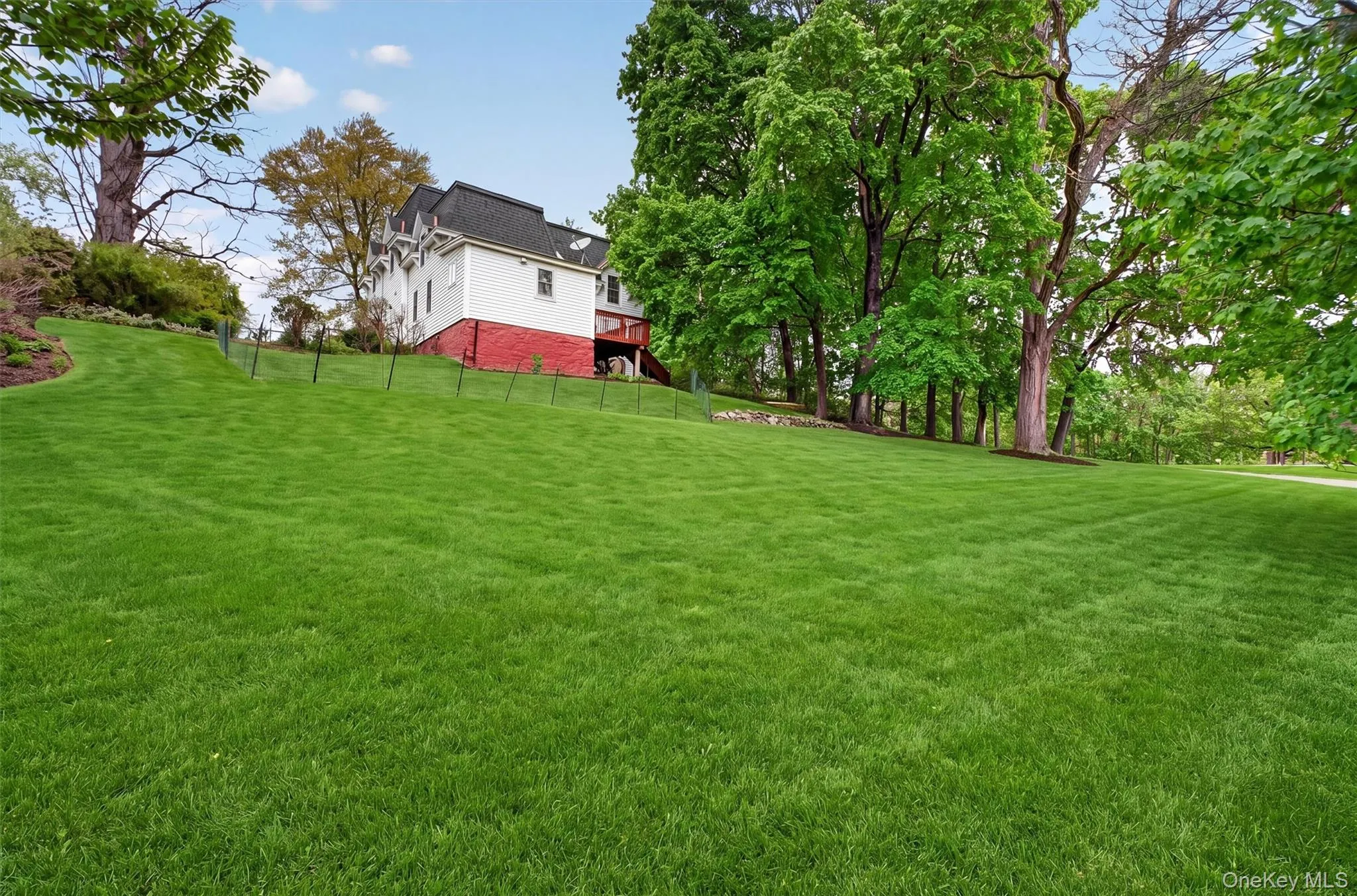 Expansive green lawn with beautiful mature trees and a colonial structure featuring white siding and a red foundation. Expansive green lawn with beautiful mature trees and a colonial structure featuring white siding and a red foundation.