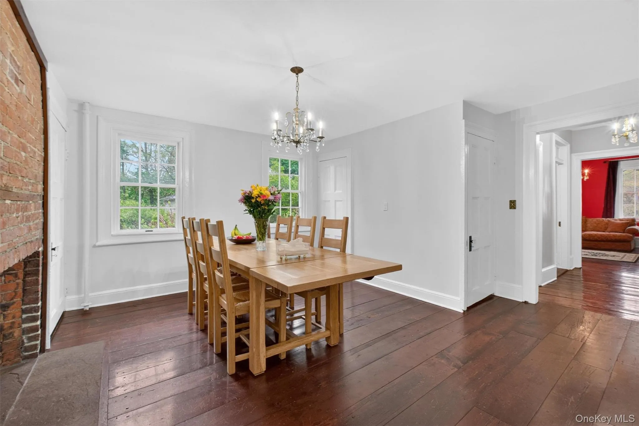 Dining room featuring a prominent exposed brick fireplace, hardwood flooring, large windows and a doorway leading other living areas. Dining room featuring a prominent exposed brick fireplace, hardwood flooring, large windows and a doorway leading other living areas.