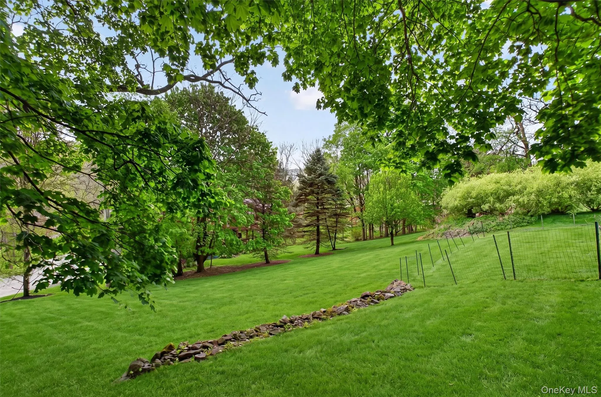 Expansive green lawn with mature trees and a stone-lined wall. Expansive green lawn with mature trees and a stone-lined wall.