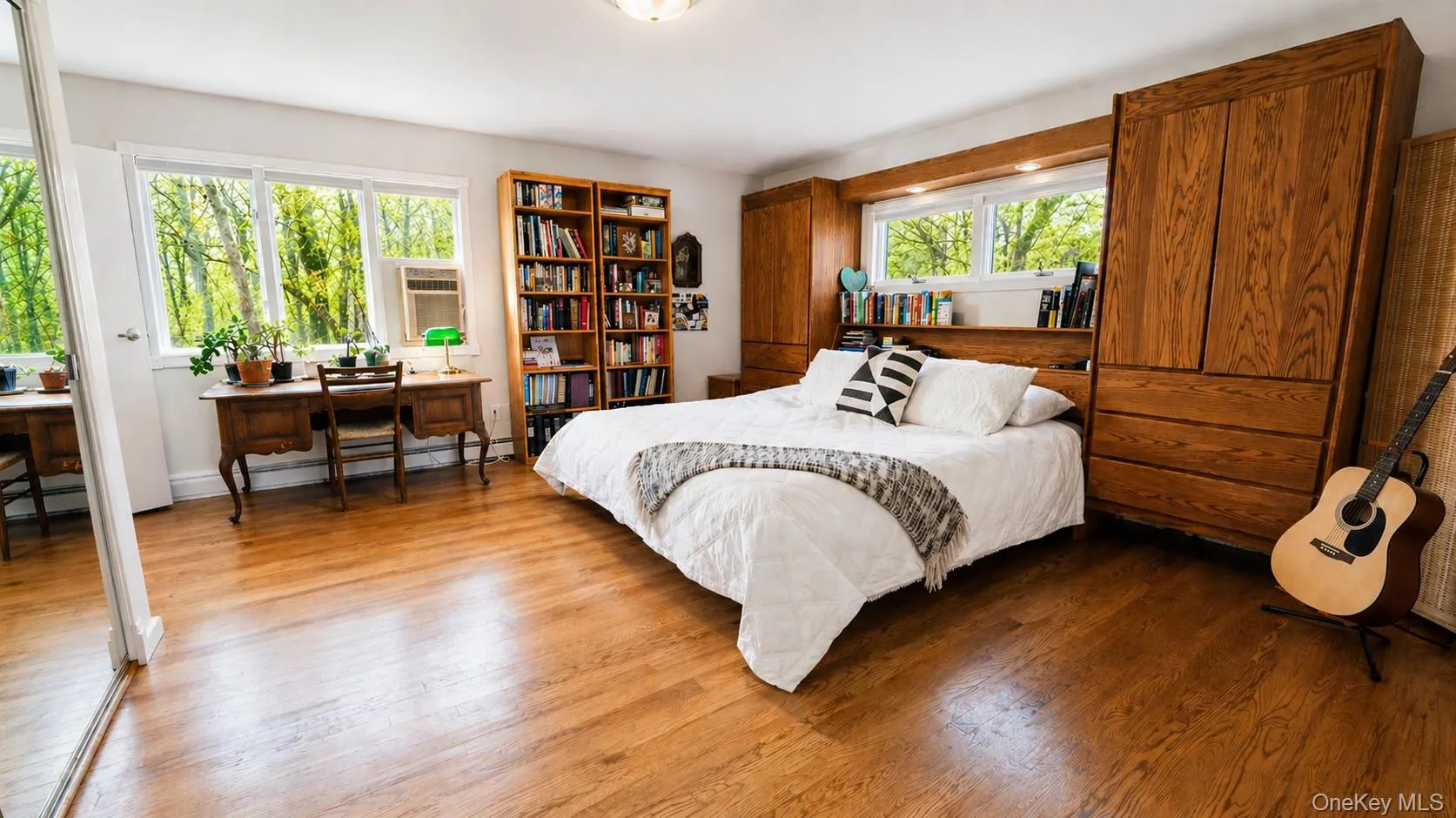 The expansive primary bedroom features hardwood flooring, beautiful natural light, and windows that showcase serene views of nature. The expansive primary bedroom features hardwood flooring, beautiful natural light, and windows that showcase serene views of nature.