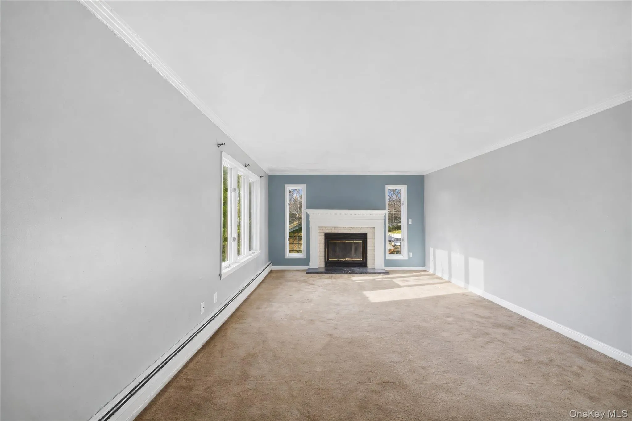 Room featuring a stone fireplace with a white mantel, beige carpet flooring, and white crown molding Room featuring a stone fireplace with a white mantel, beige carpet flooring, and white crown molding