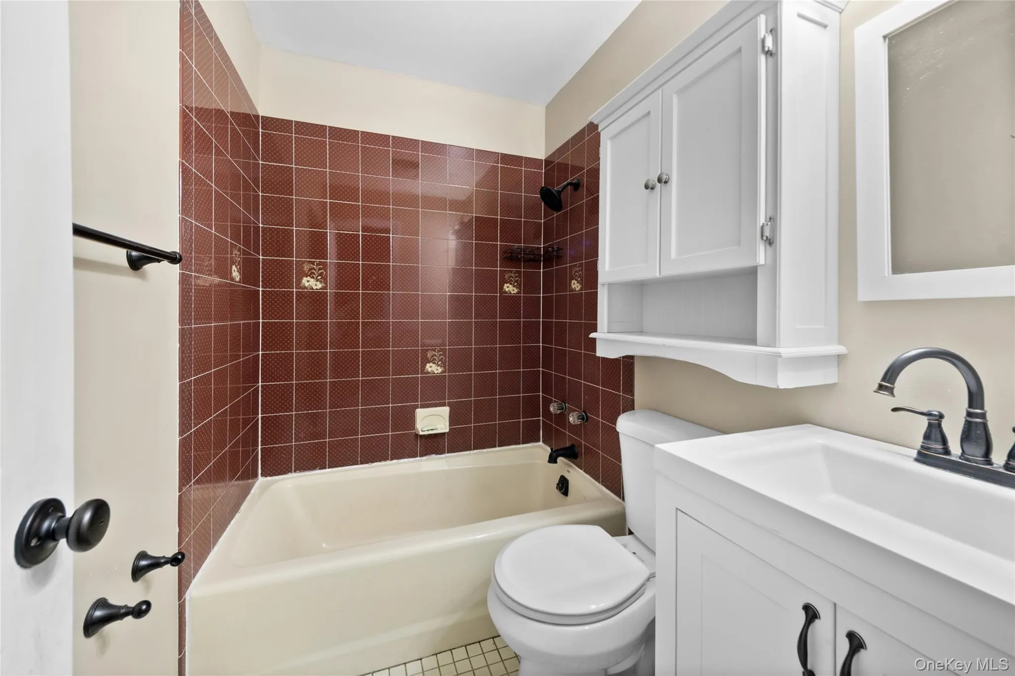 Bathroom featuring a white vanity with a dark bronze faucet, a matching medicine cabinet, a tiled shower-tub combination, and a white toilet Bathroom featuring a white vanity with a dark bronze faucet, a matching medicine cabinet, a tiled shower-tub combination, and a white toilet