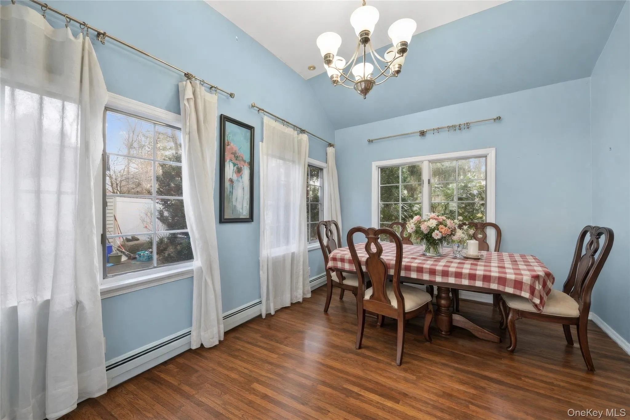Dining area featuring vaulted ceilings, wood-finish flooring, a multi-light chandelier, and multiple paneled windows Dining area featuring vaulted ceilings, wood-finish flooring, a multi-light chandelier, and multiple paneled windows