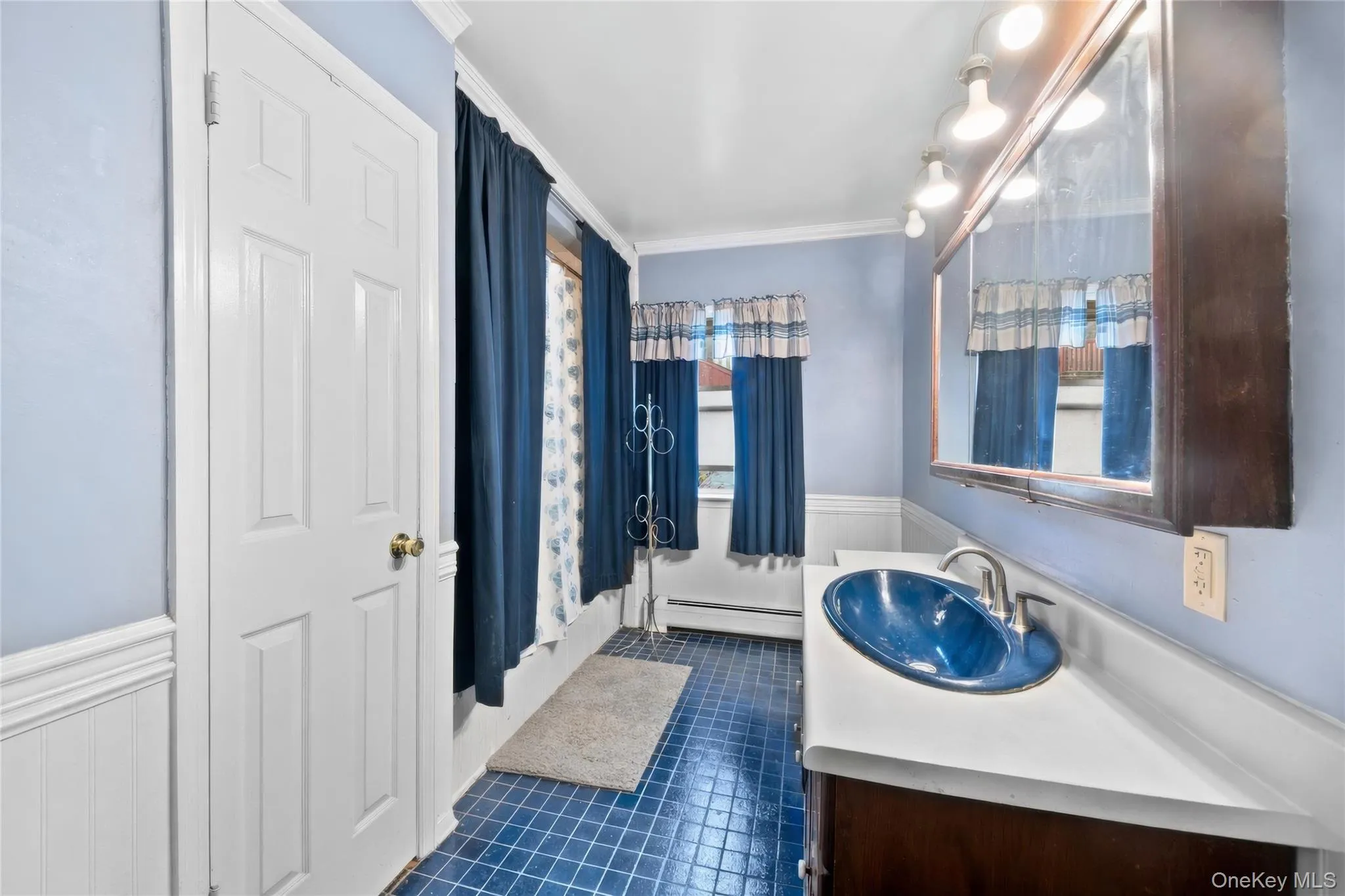 Bathroom featuring a blue tile floor, white wainscoting, white countertop, and a dark wood vanity with an oval blue sink Bathroom featuring a blue tile floor, white wainscoting, white countertop, and a dark wood vanity with an oval blue sink