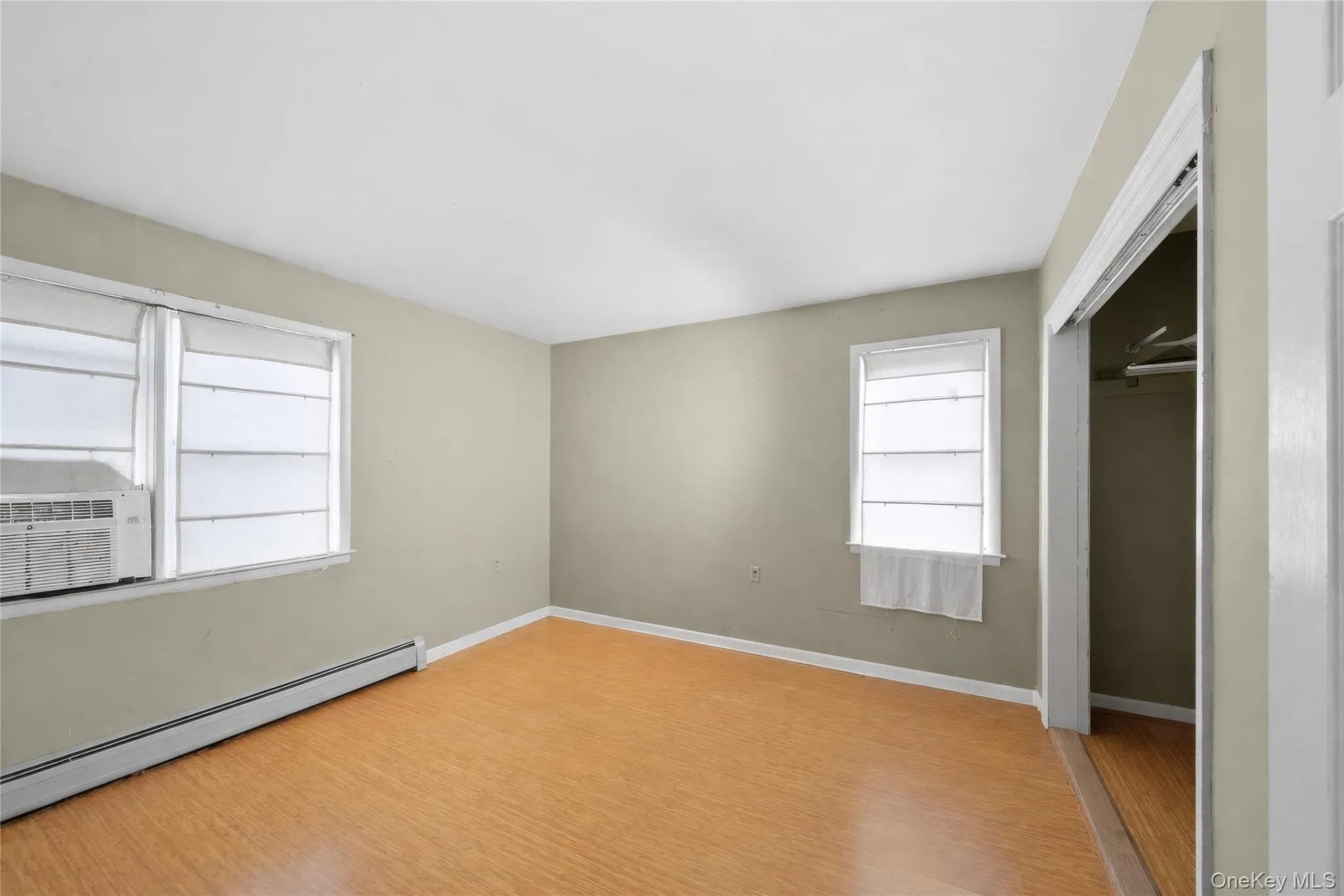Room featuring wood-finish flooring, two windows, and neutral wall paint Room featuring wood-finish flooring, two windows, and neutral wall paint